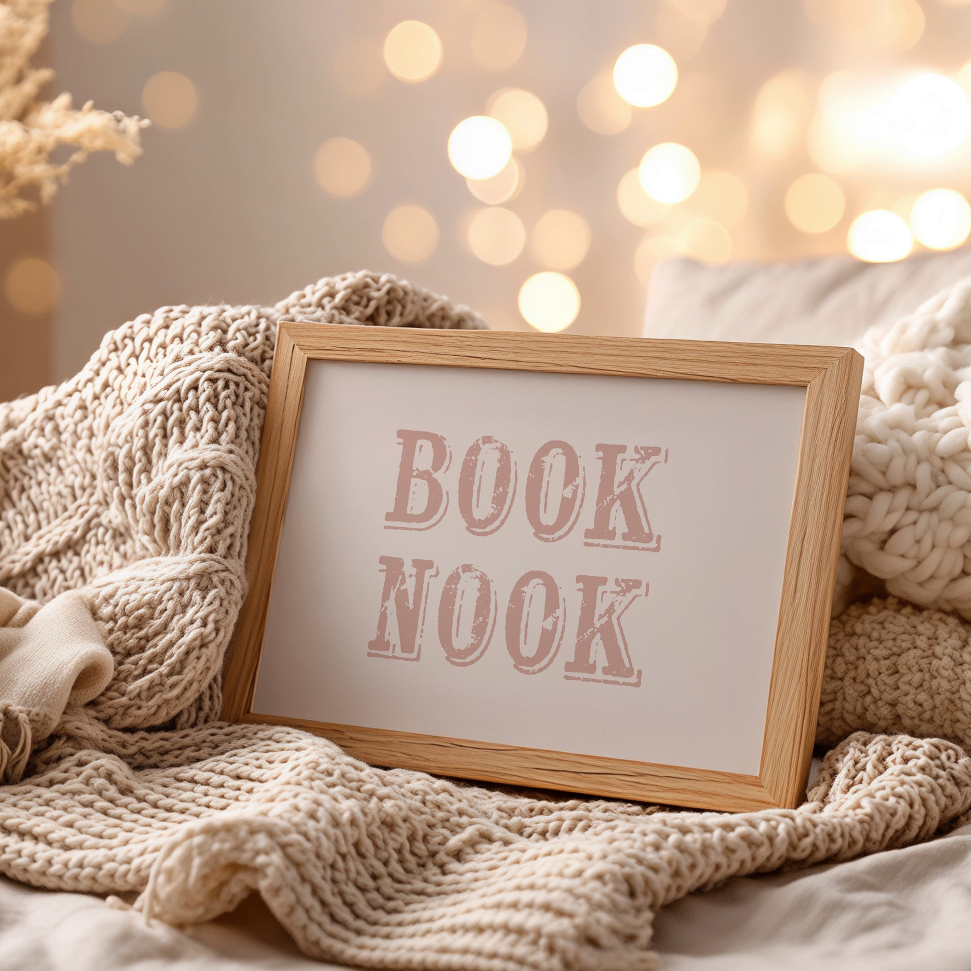 Framed wall art with 'BOOK NOOK' text on a cozy blanket with blurred lights in the background
