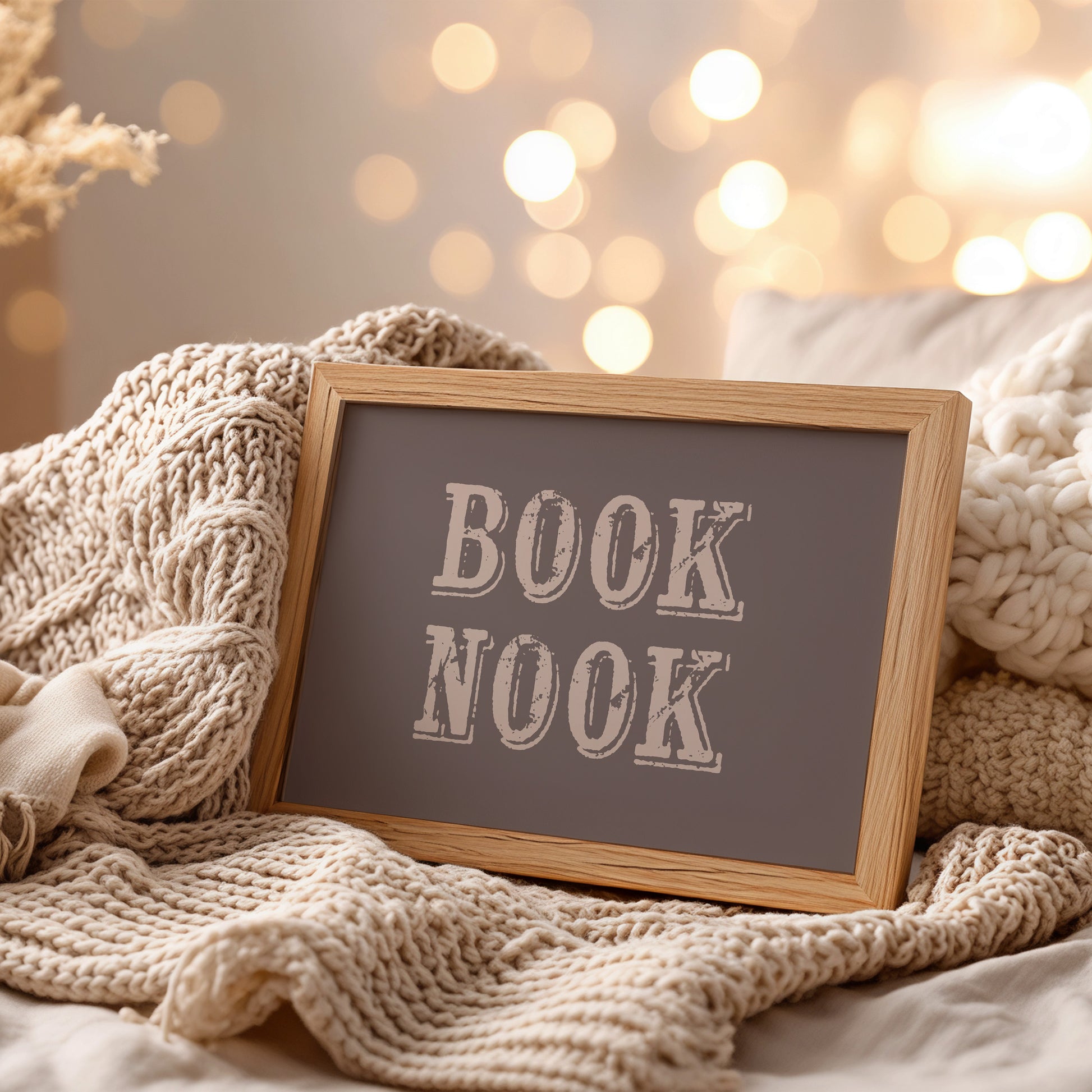 Frame wall art print with 'BOOK NOOK' text on a cozy setting with knitted textures and soft lighting.