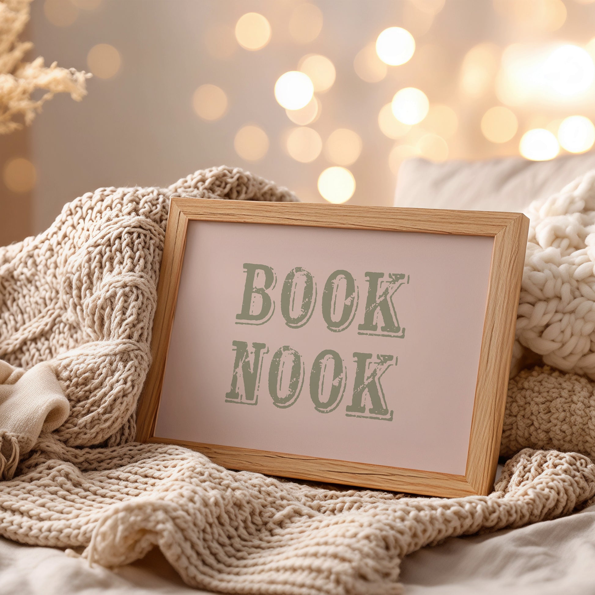 Framed wall art with 'BOOK NOOK' text on a cozy blanket with blurred lights in the background