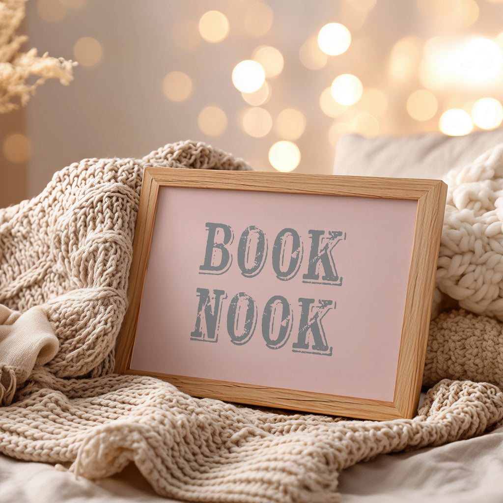 Framed wall art with 'BOOK NOOK' text on a cozy blanket with blurred lights in the background