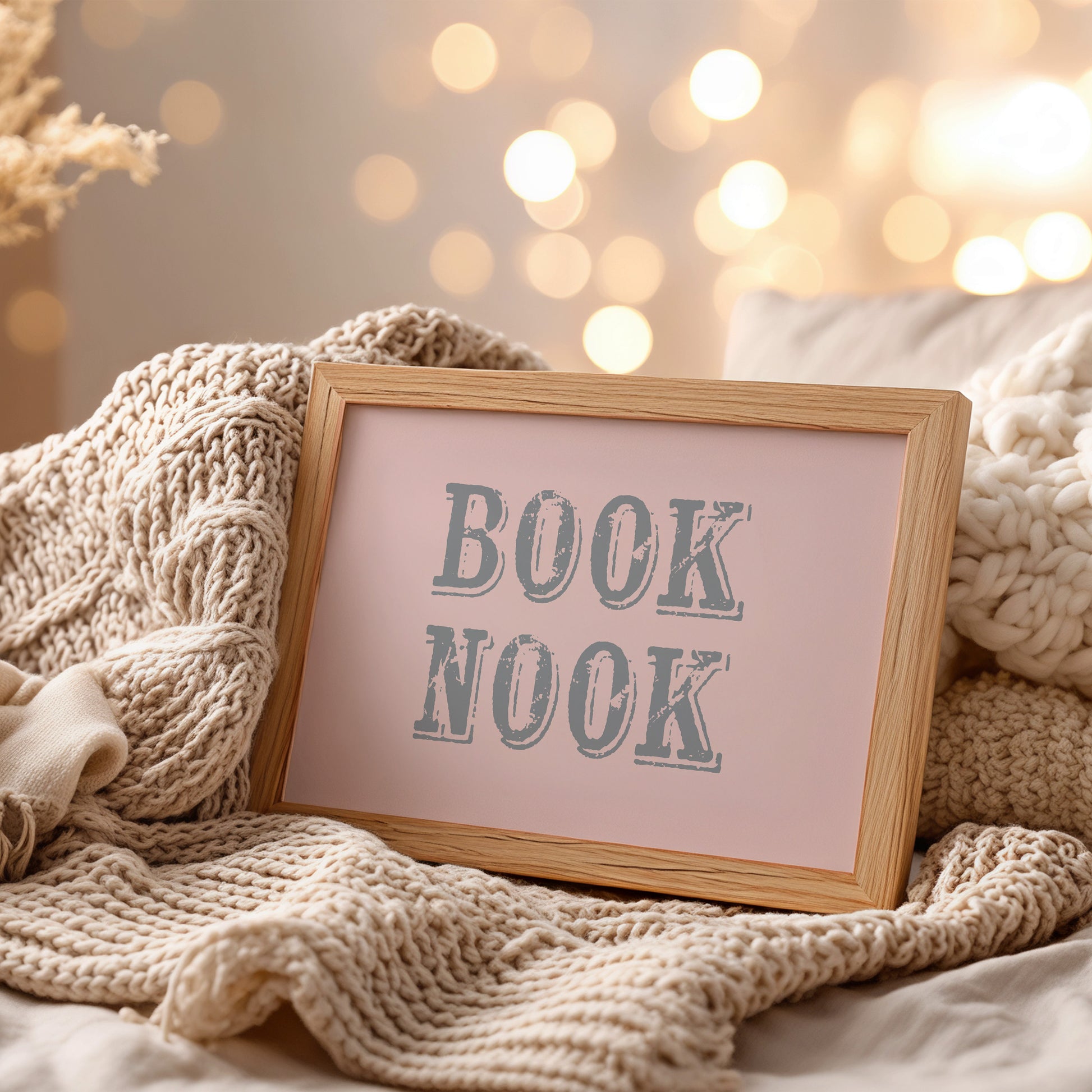 Framed wall art with 'BOOK NOOK' text on a cozy blanket with blurred lights in the background