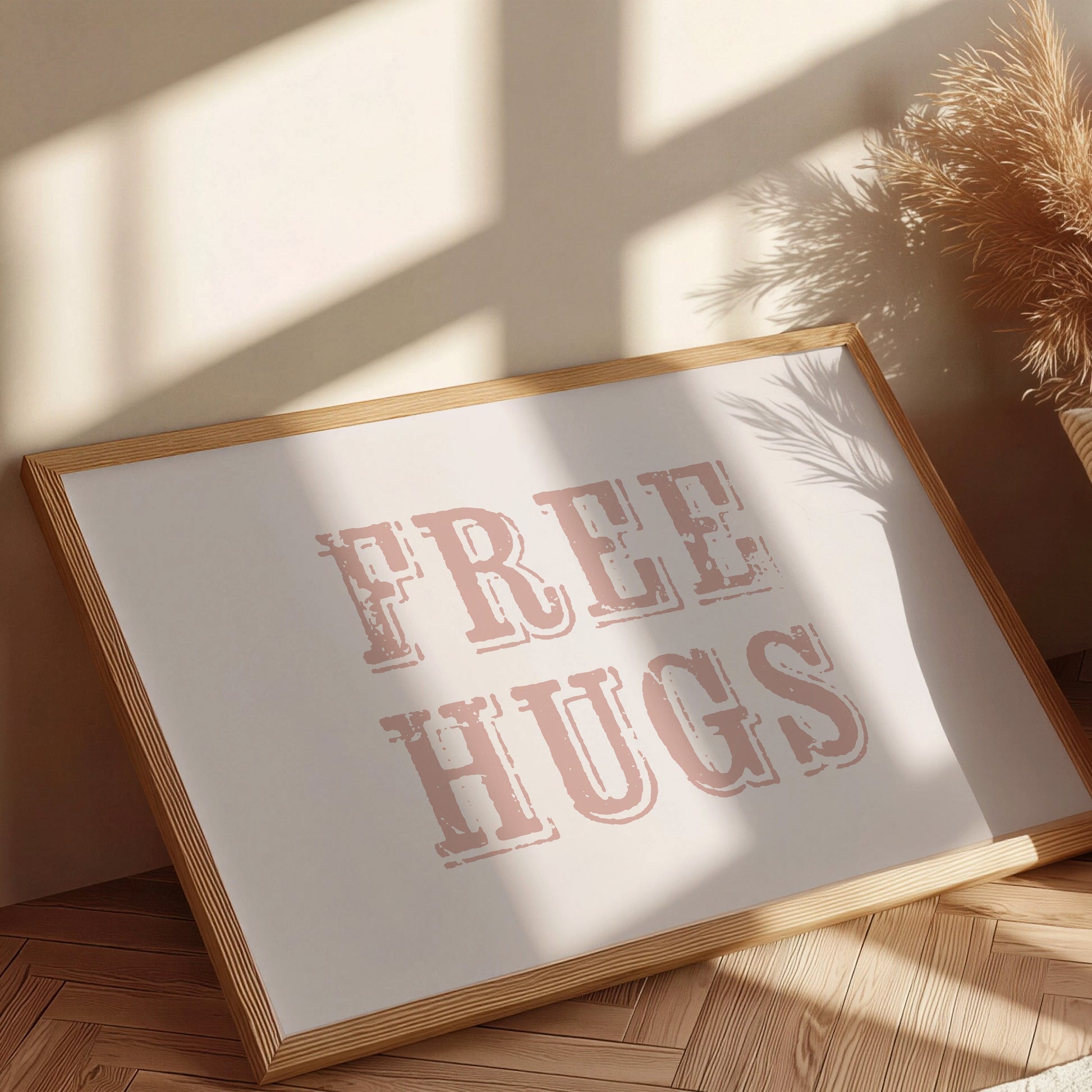 Framed artwork with 'FREE HUGS' text on a wooden floor with sunlight casting shadows.