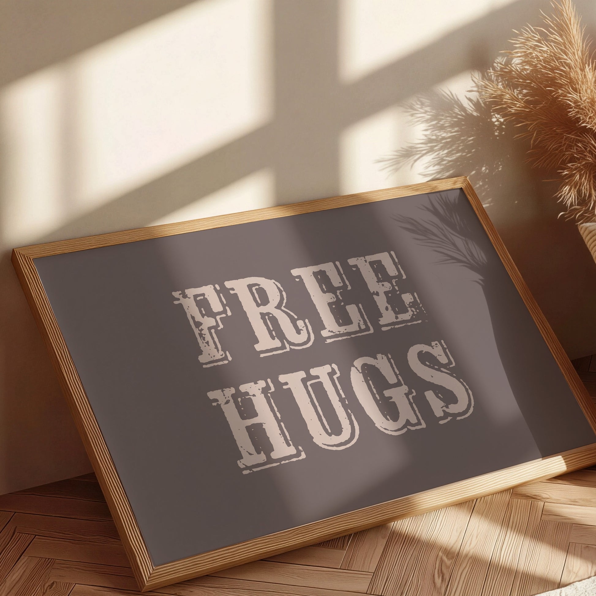 Framed sign with 'FREE HUGS' text on a wooden floor with sunlight casting shadows.