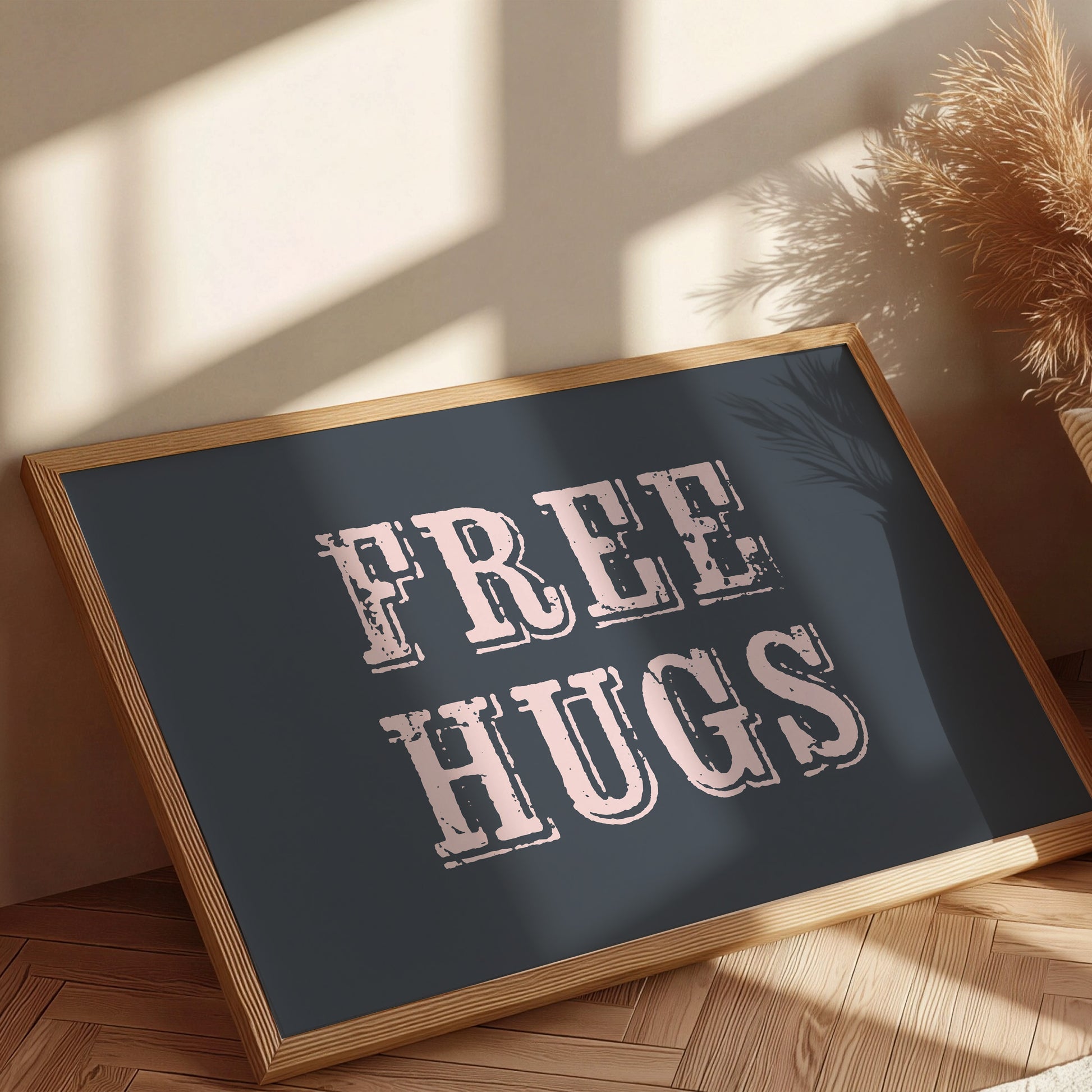 Framed sign with 'FREE HUGS' text on a wooden floor with sunlight casting shadows.