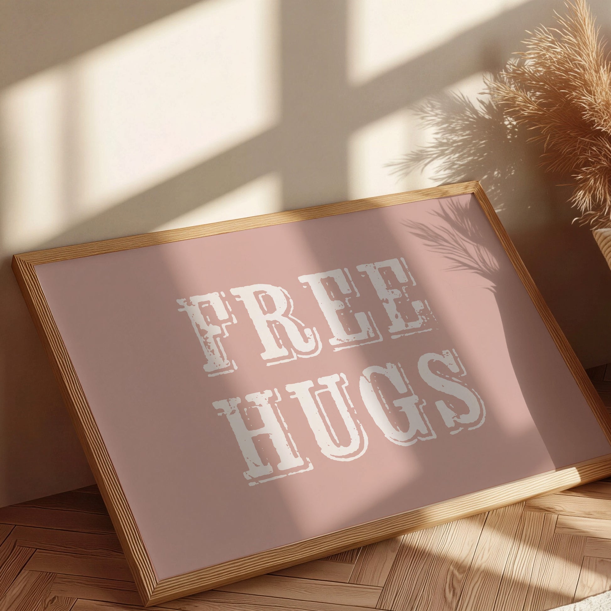 Framed sign with 'FREE HUGS' text on a wooden floor with sunlight casting shadows.