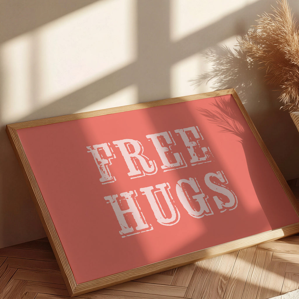 Framed sign with 'FREE HUGS' text on a coral background, placed indoors with sunlight casting shadows.