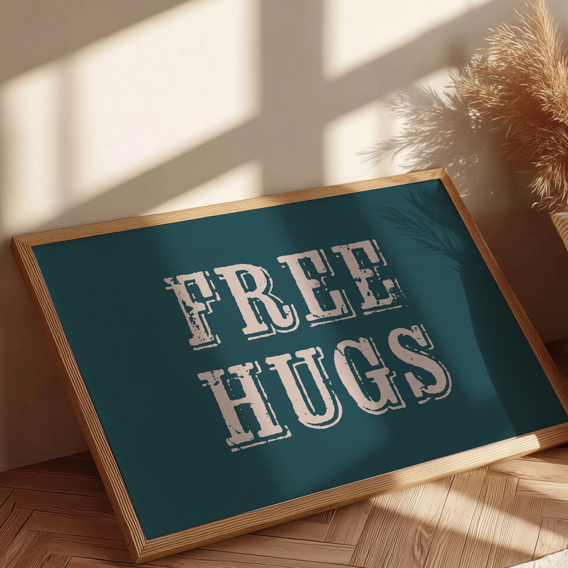 Framed sign with 'FREE HUGS' text on a teal background, placed indoors with sunlight casting shadows.