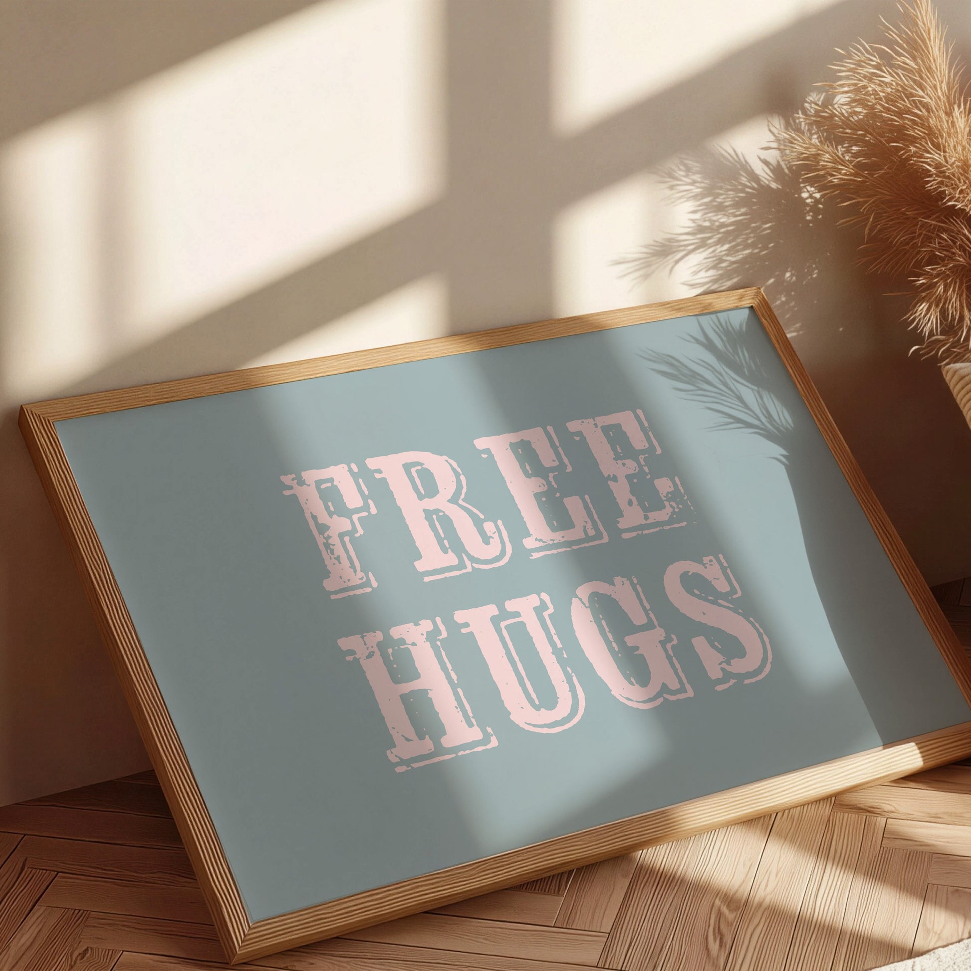 Framed sign with 'FREE HUGS' text on a wooden floor with sunlight casting shadows.