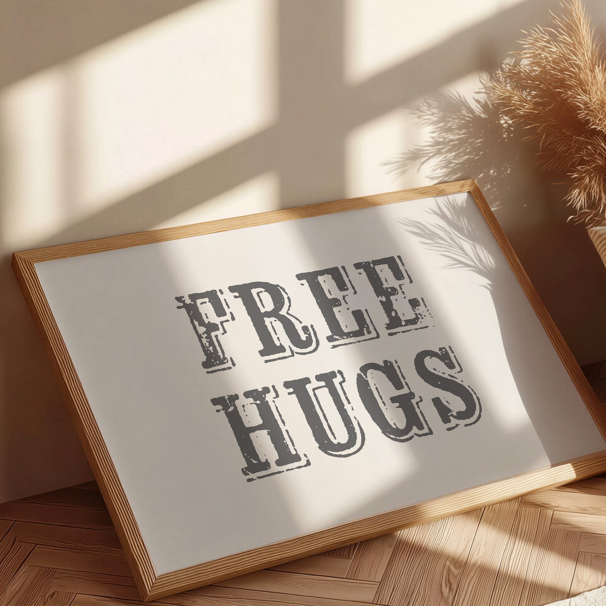 Framed sign with 'FREE HUGS' text on a wooden floor with sunlight casting shadows.