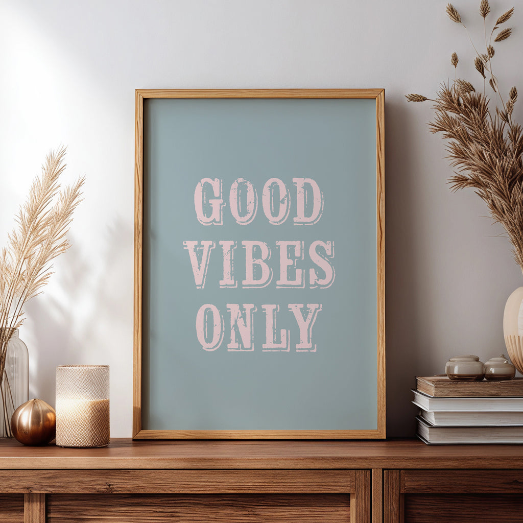 Framed artwork with 'Good Vibes Only' text on a wooden sideboard with decorative items.