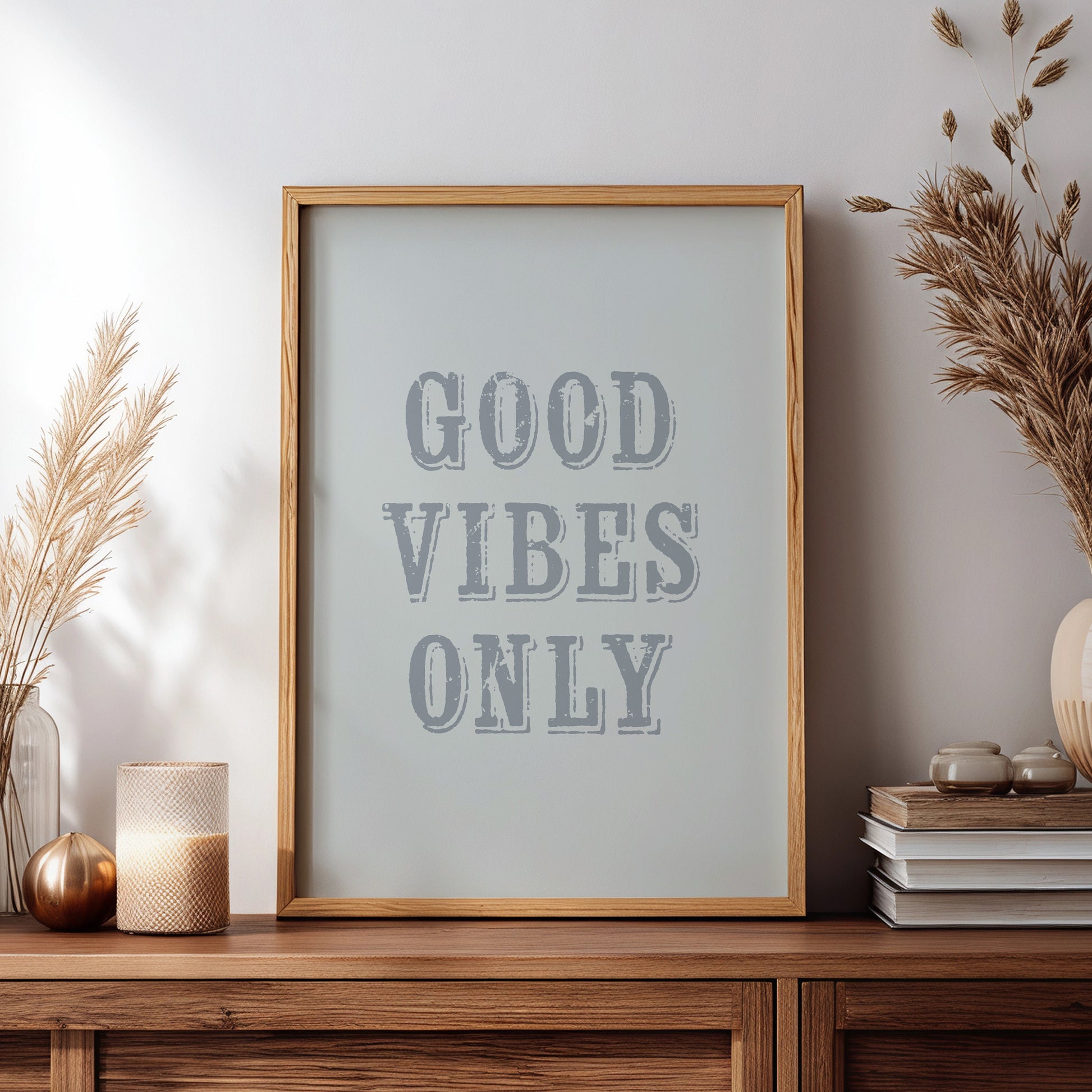 Framed artwork with 'Good Vibes Only' text on a wooden sideboard with decorative items.