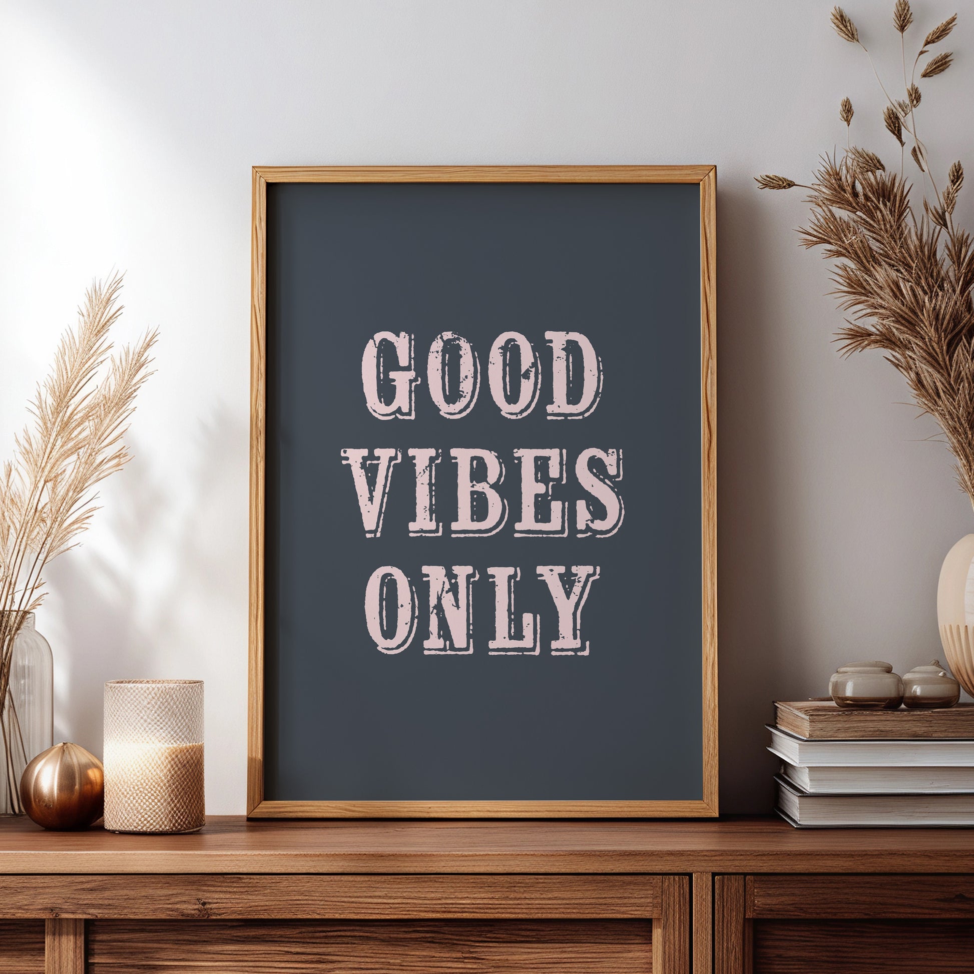 Framed poster with 'Good Vibes Only' text on a wooden sideboard with decorative items.