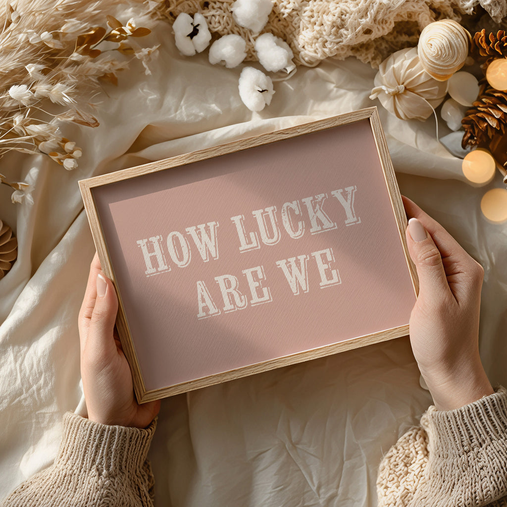 Framed sign with 'HOW LUCKY ARE WE' text held by hands against a decorative background.