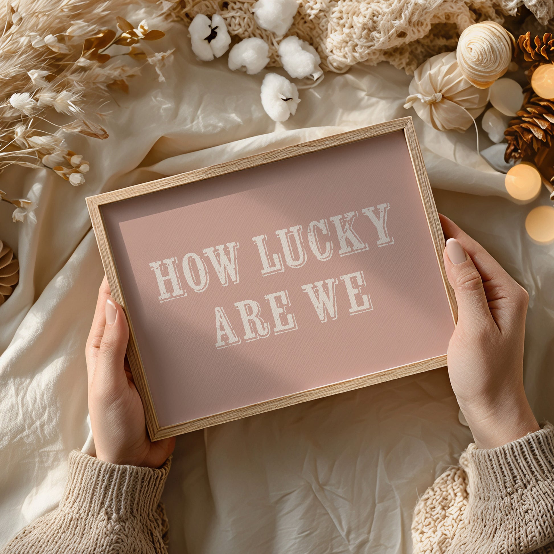 Framed sign with 'HOW LUCKY ARE WE' text held by hands against a decorative background.
