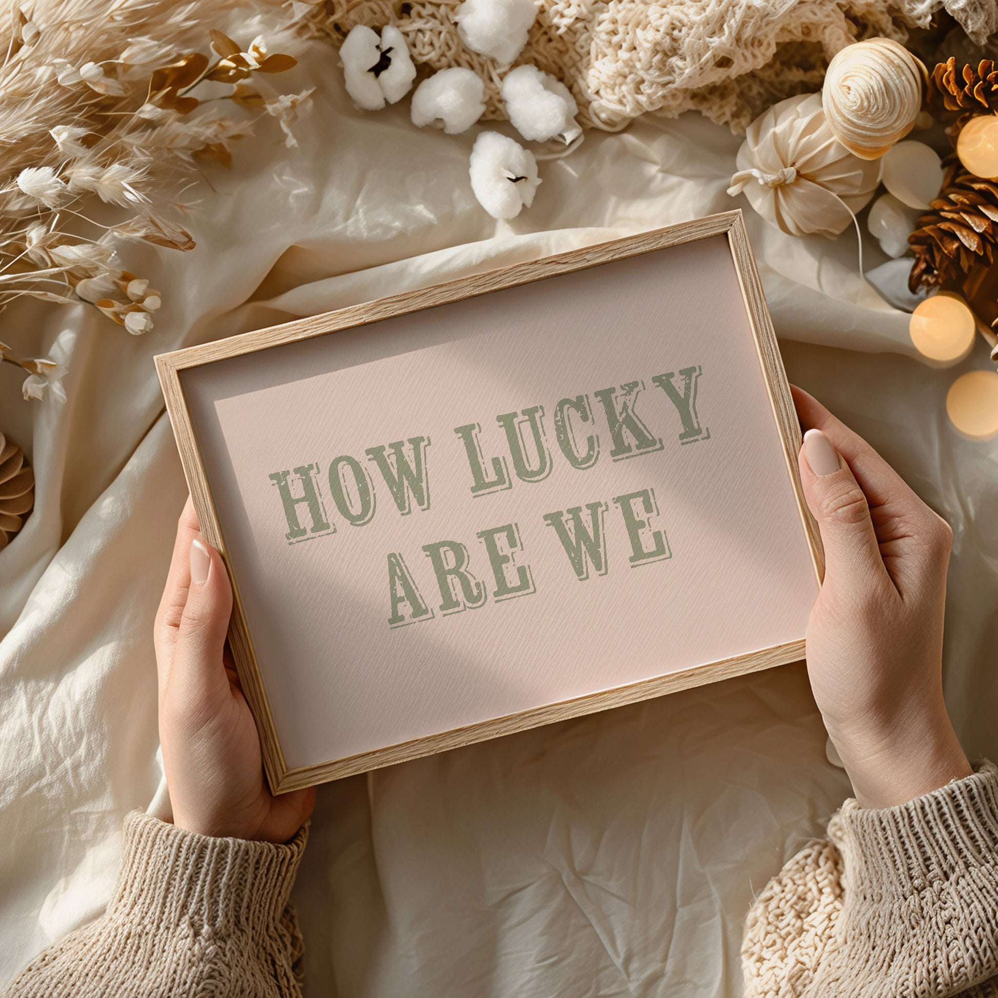 Framed sign with 'HOW LUCKY ARE WE' text held by hands against a soft, decorative background.