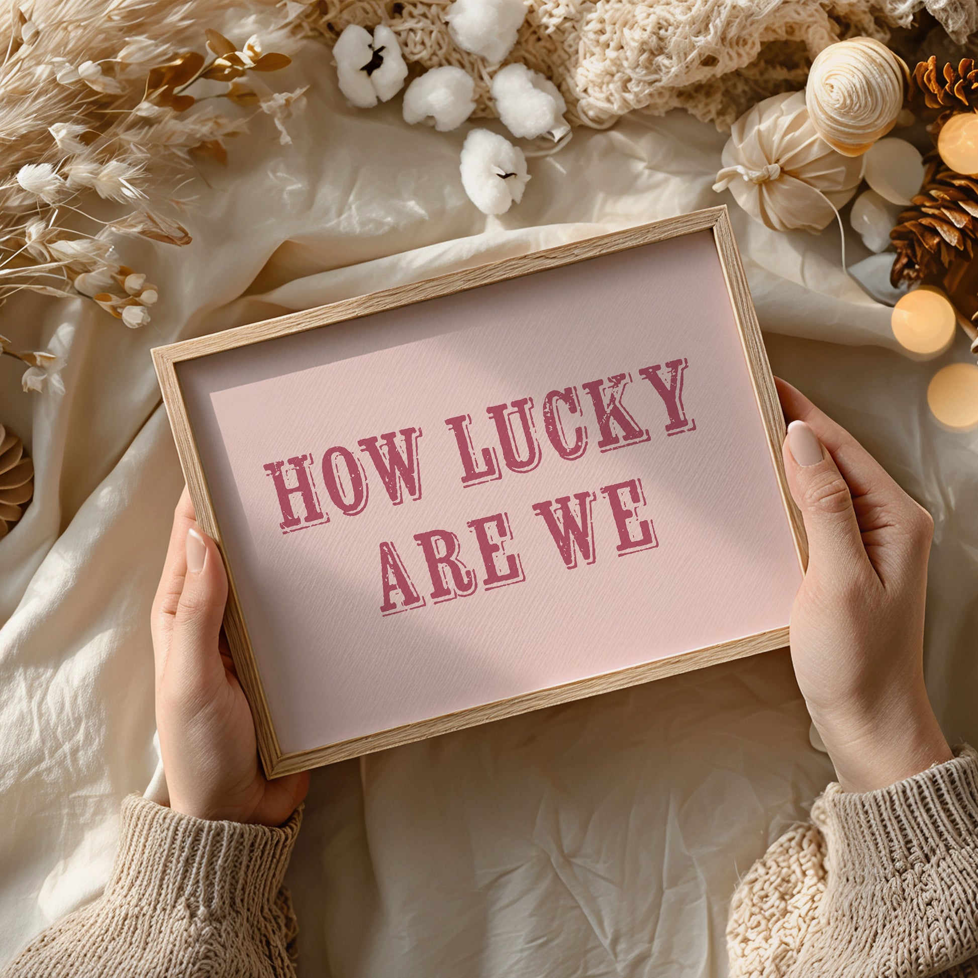Framed art print with 'HOW LUCKY ARE WE' text held by hands against a decorative background.