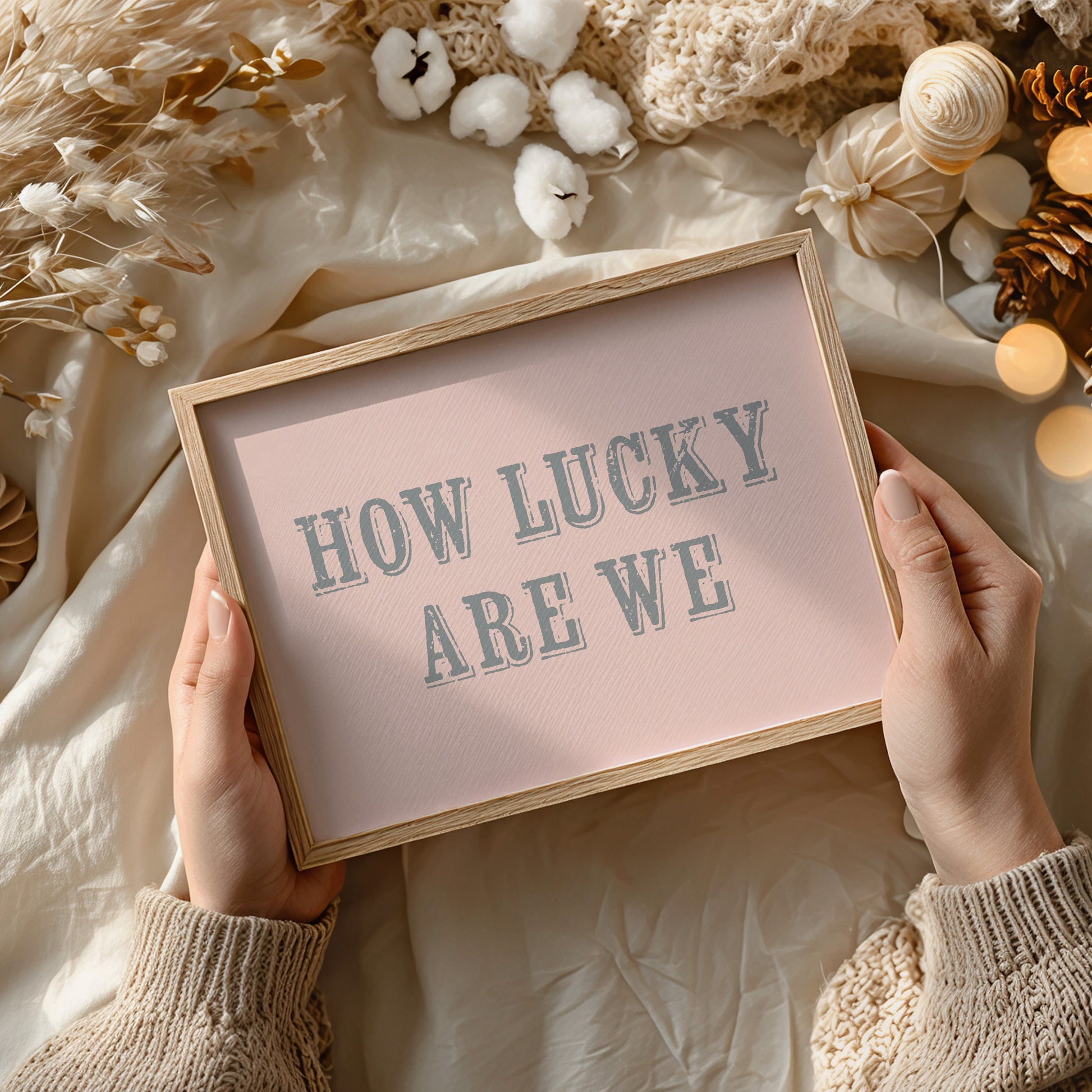 Framed art print with 'HOW LUCKY ARE WE' text held by hands against a decorative background.