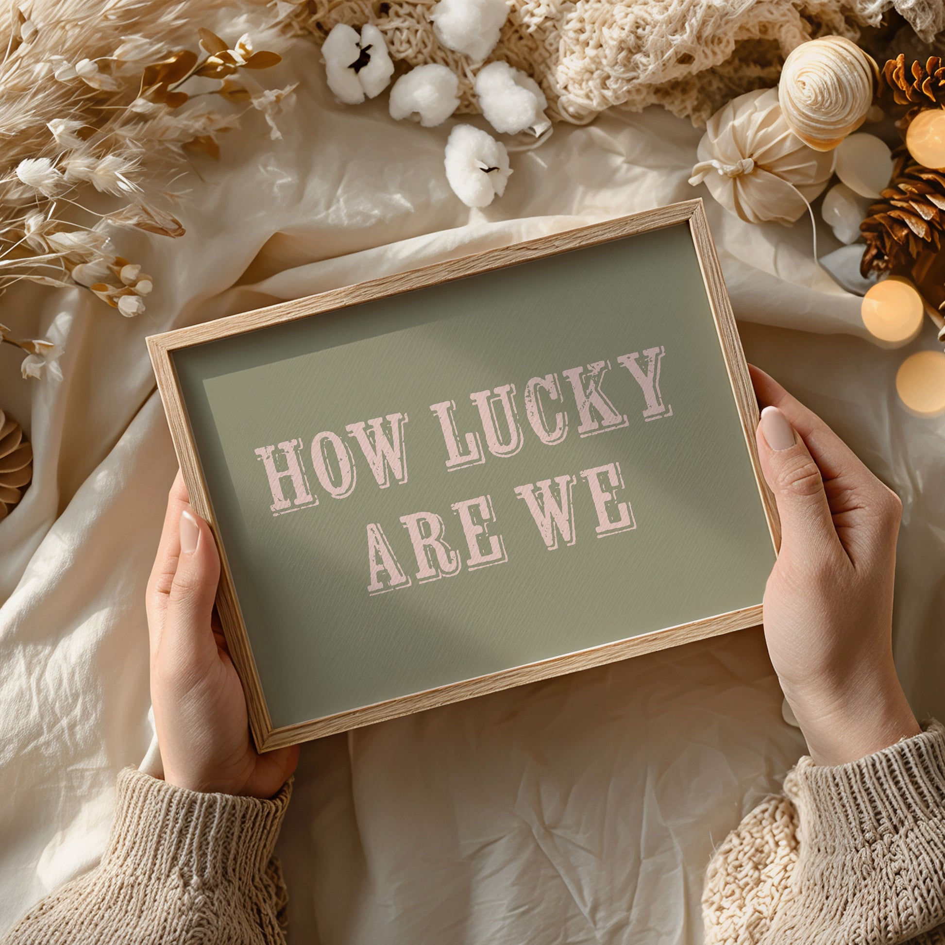 Framed sign with 'HOW LUCKY ARE WE' text held by hands against a decorative background.