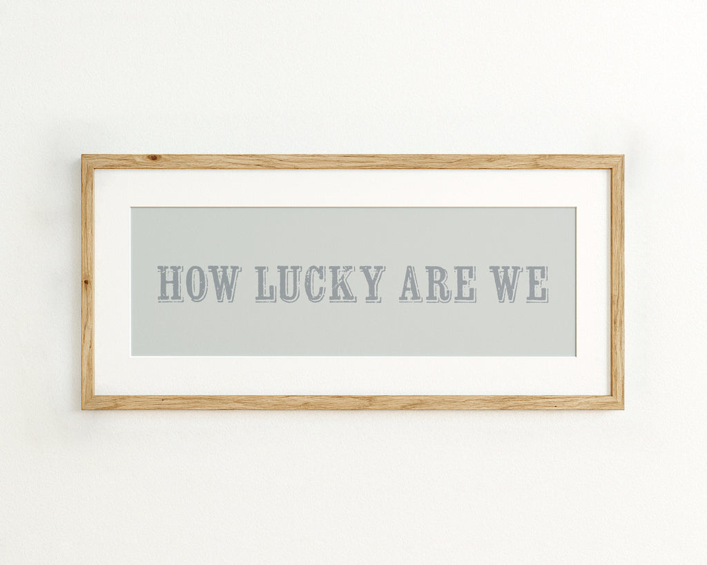 Framed print with 'HOW LUCKY ARE WE' text on a light blue background