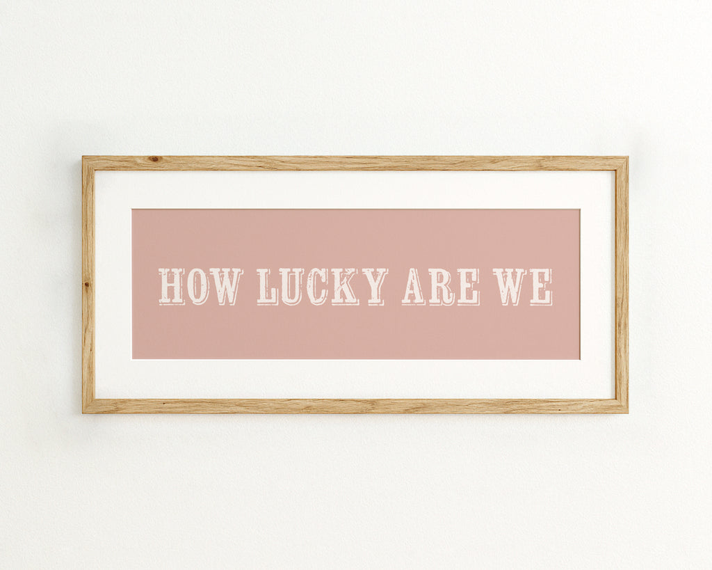 Framed print with 'HOW LUCKY ARE WE' text on a pink background