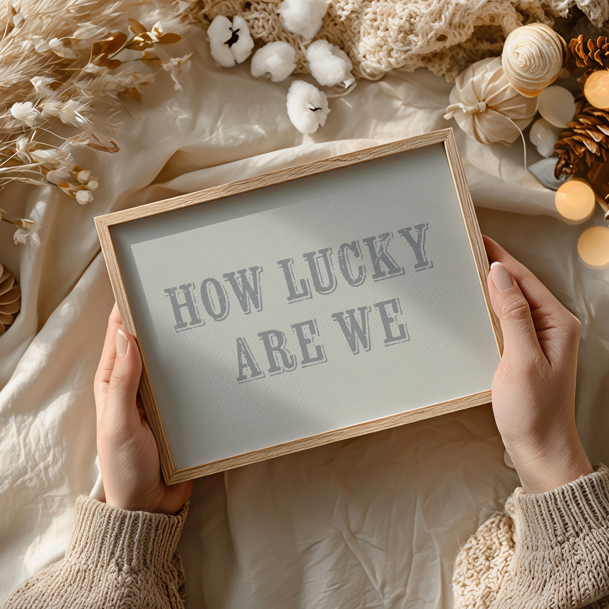 Framed art print with 'HOW LUCKY ARE WE' text held by hands against a decorative background.