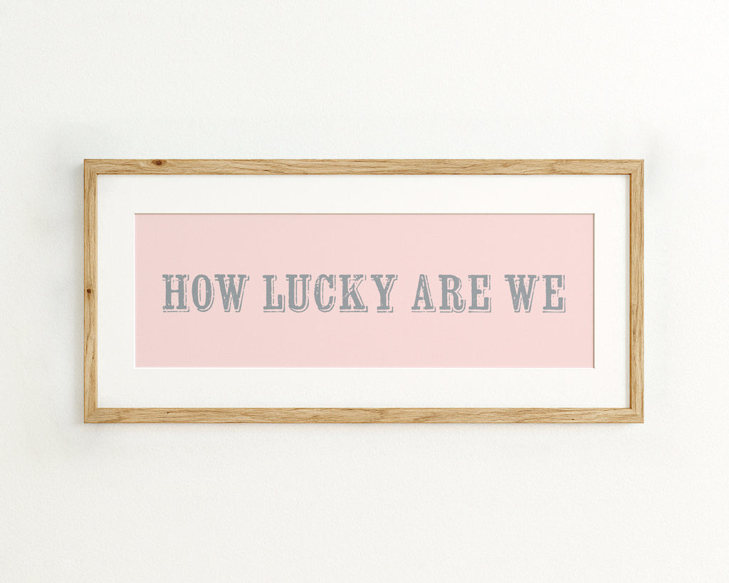 Framed print with 'HOW LUCKY ARE WE' text on a pink background