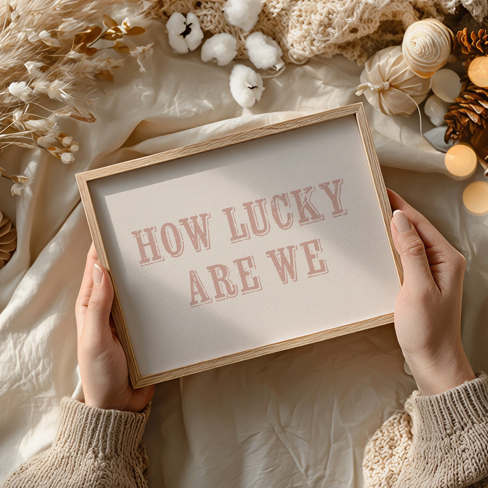 Framed sign with 'HOW LUCKY ARE WE' text held by hands against a soft, decorative background.