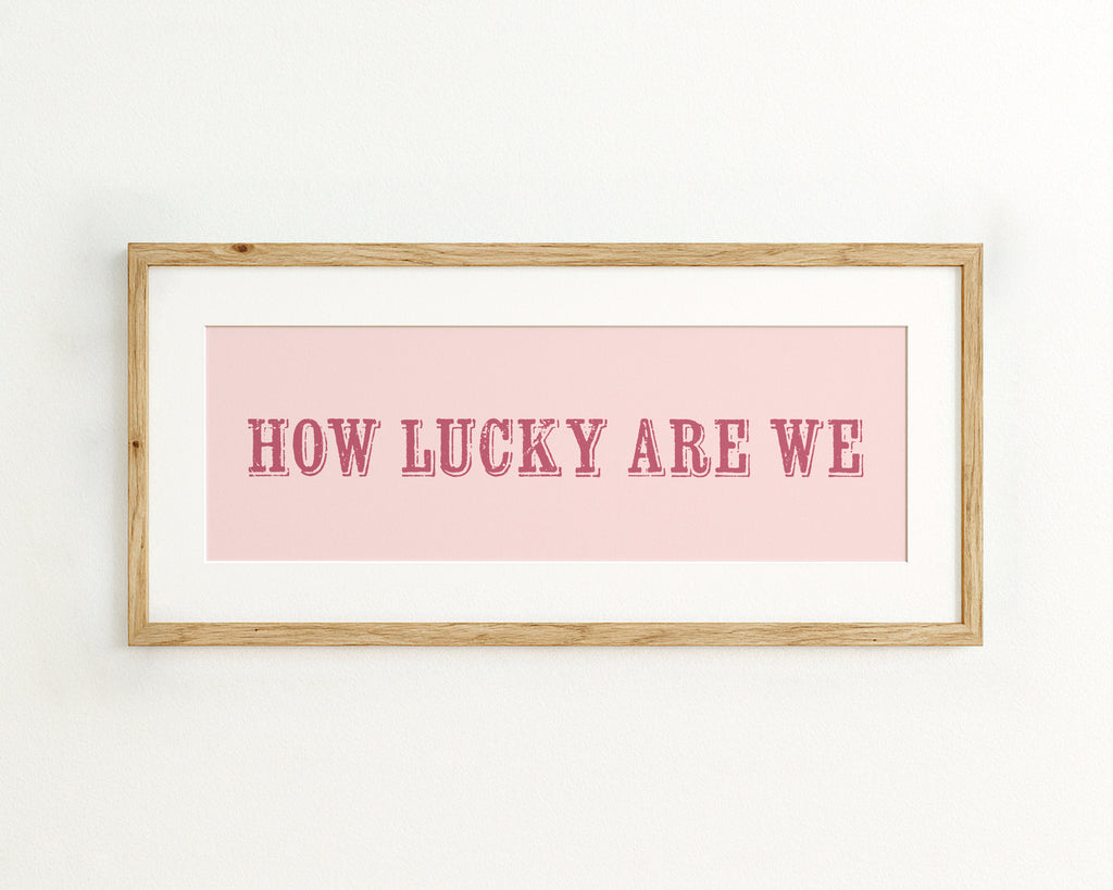 Framed print with 'HOW LUCKY ARE WE' text on a pink background