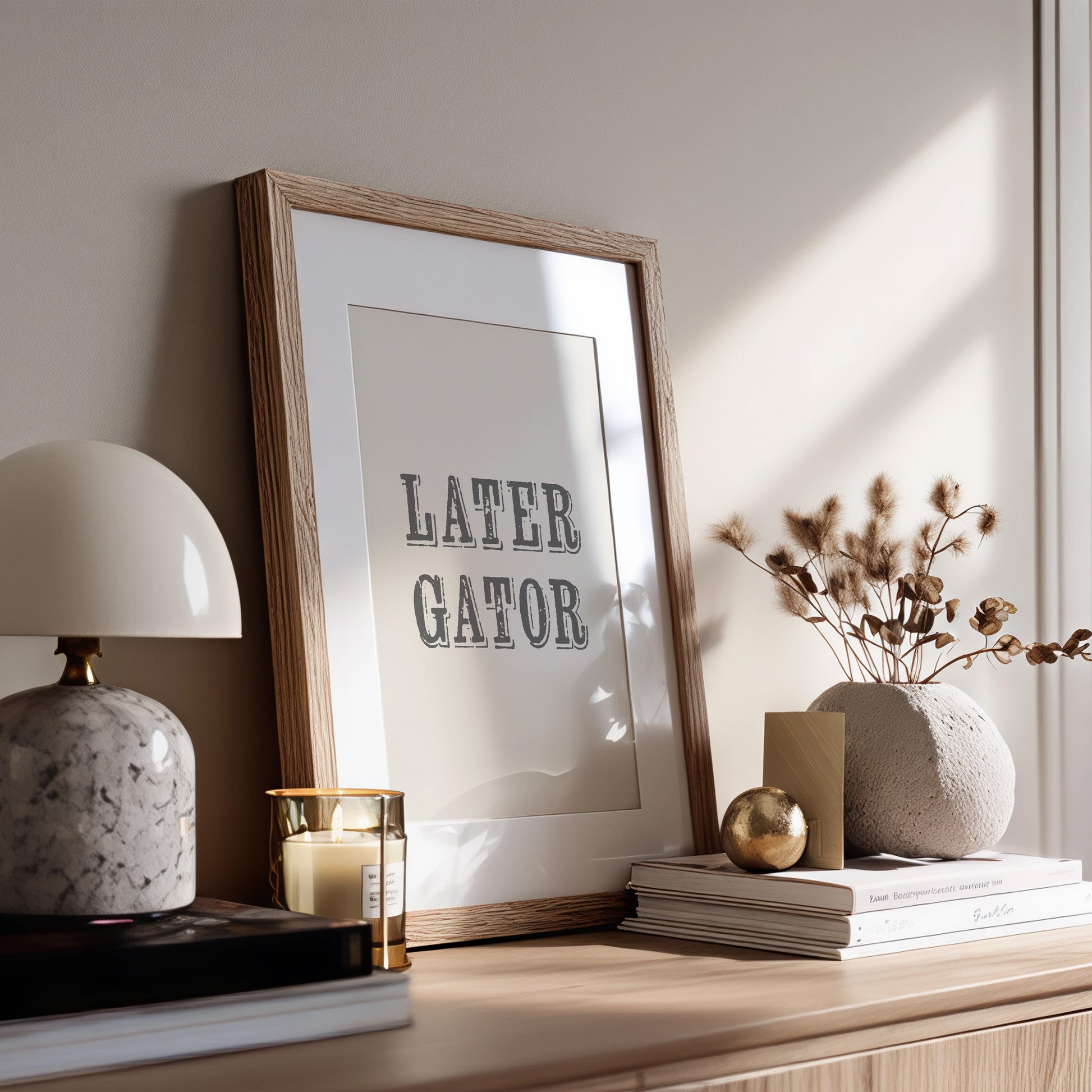 Framed artwork with 'LATER GATOR' text on a wooden surface with decorative items.
