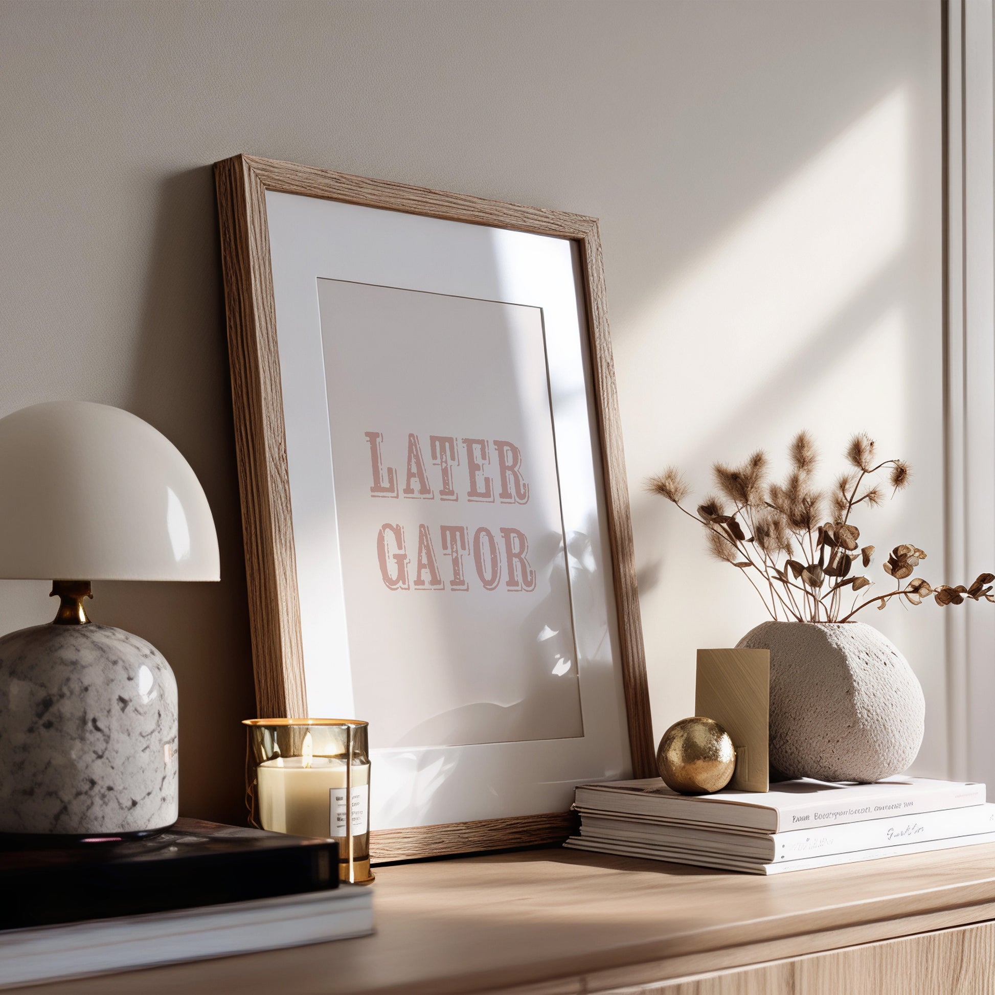 Framed print with 'LATER GATOR' text on a wooden surface with decor items.