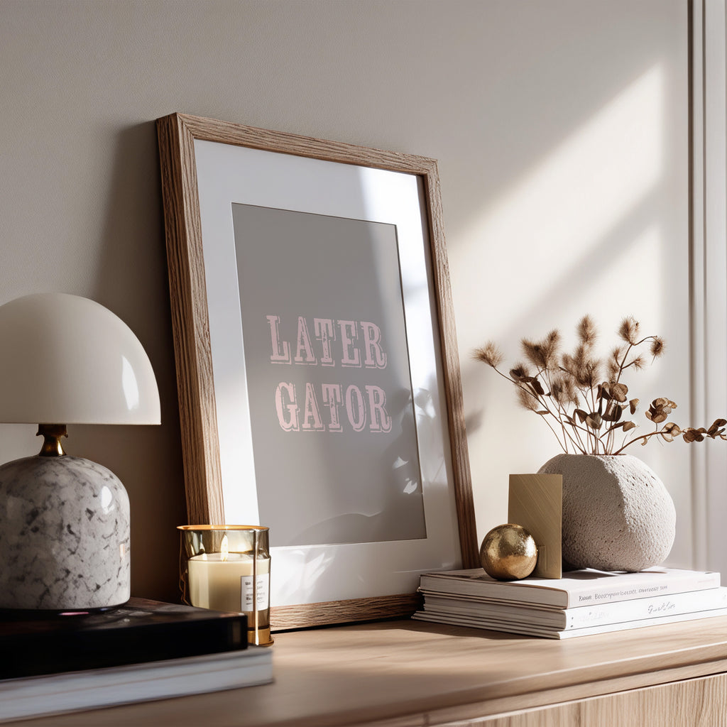 Framed print with 'LATER GATOR' text on a wooden surface with decor items.