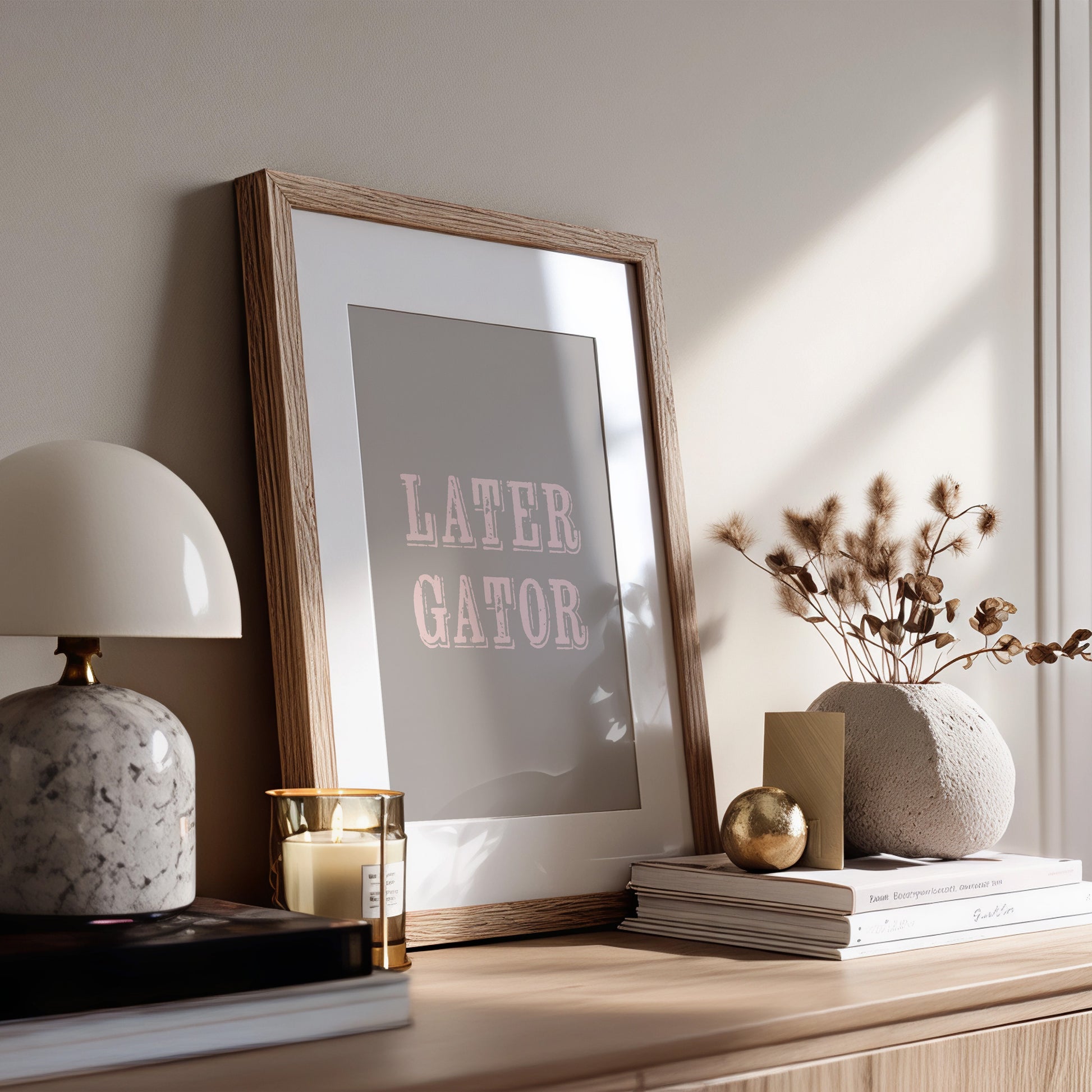 Framed print with 'LATER GATOR' text on a wooden surface with decor items.