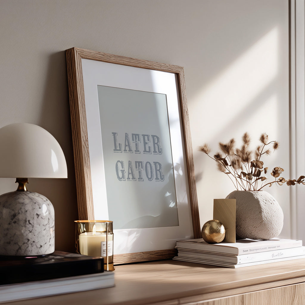 Framed artwork with 'LATER GATOR' text on a wooden surface with decorative items.