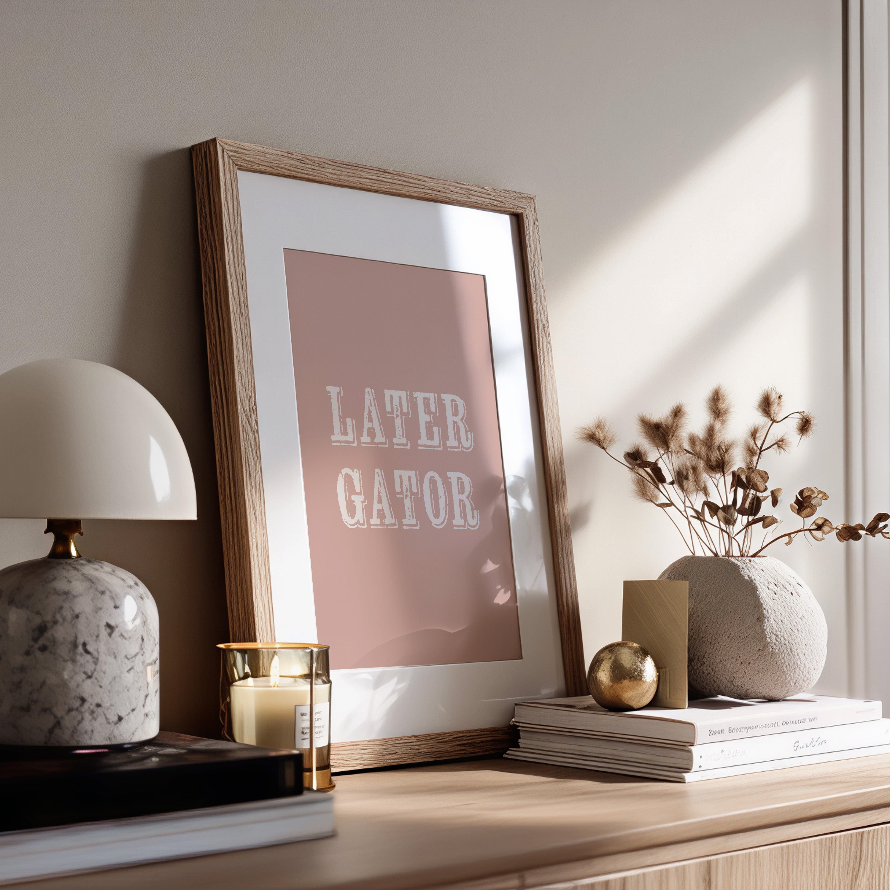 Framed print with 'LATER GATOR' text on a wooden surface with decor items.
