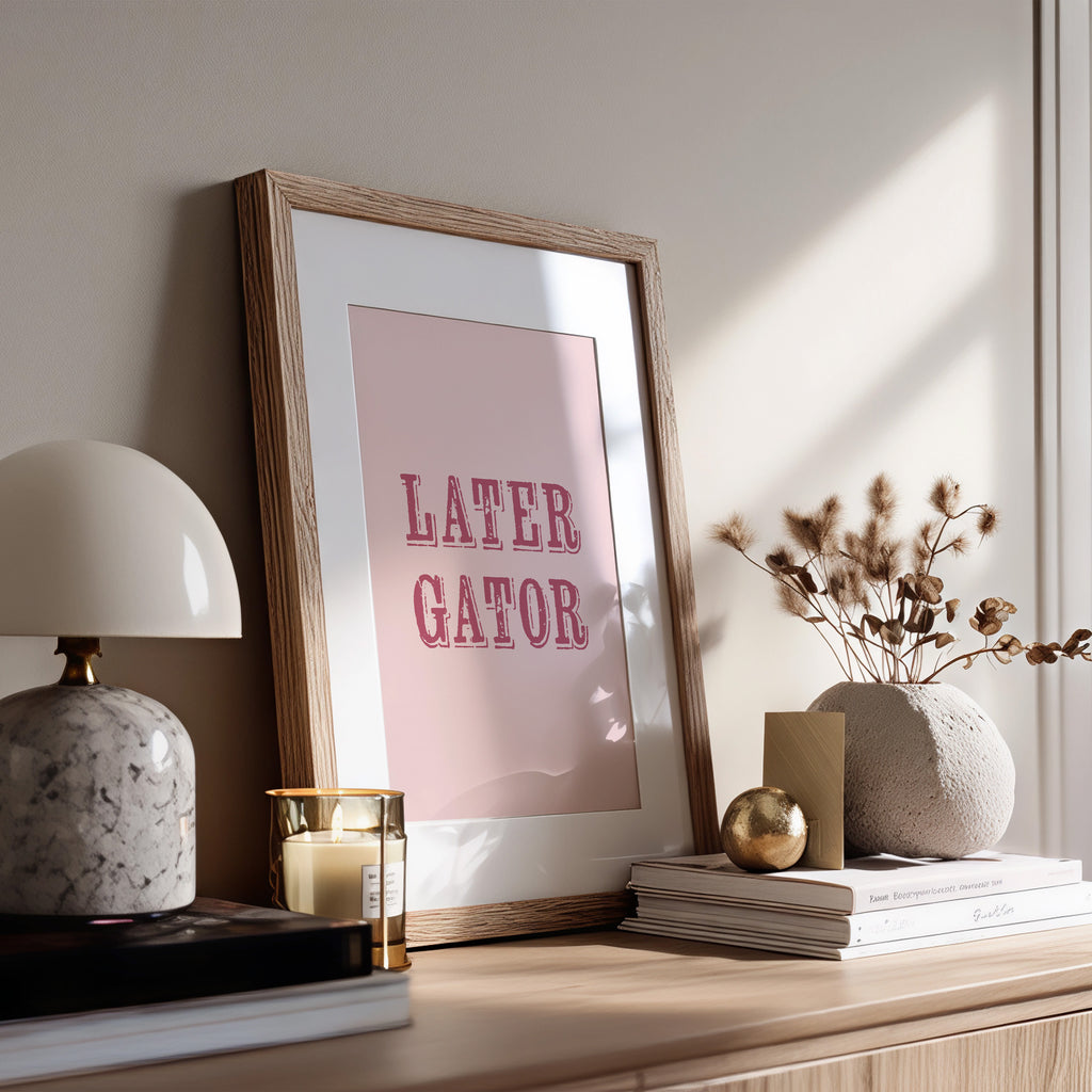 Framed print with 'LATER GATOR' text on a shelf with decor items