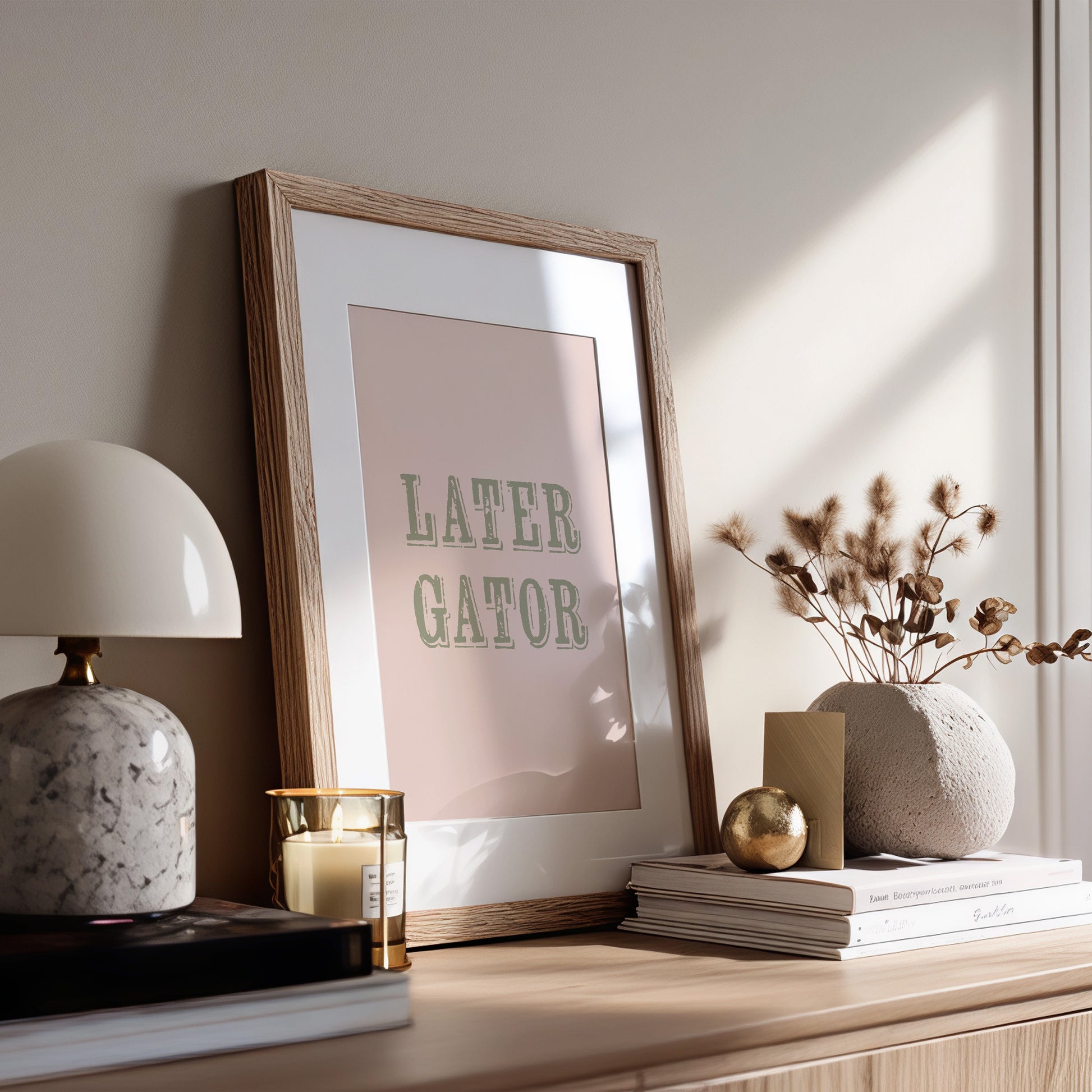 Framed print with 'LATER GATOR' text on a wooden surface with decor items.