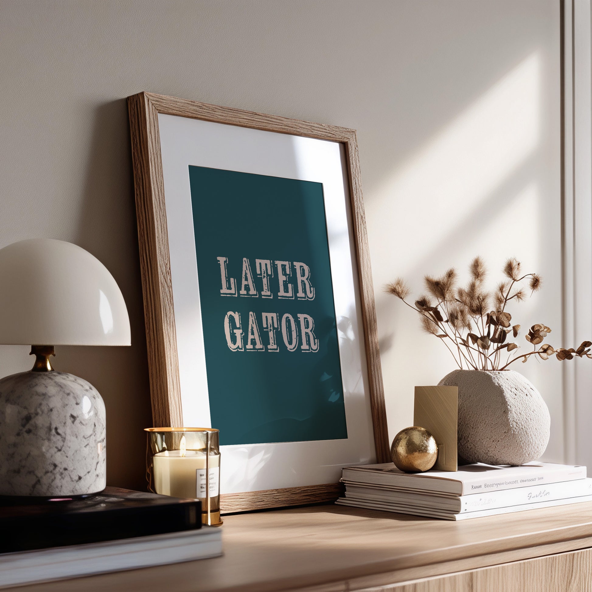 Framed print with 'LATER GATOR' text on a wooden surface with decor items.
