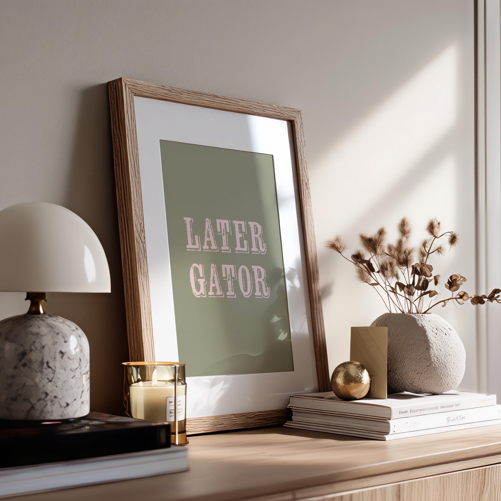Framed print with 'LATER GATOR' text on a wooden surface with decor items.