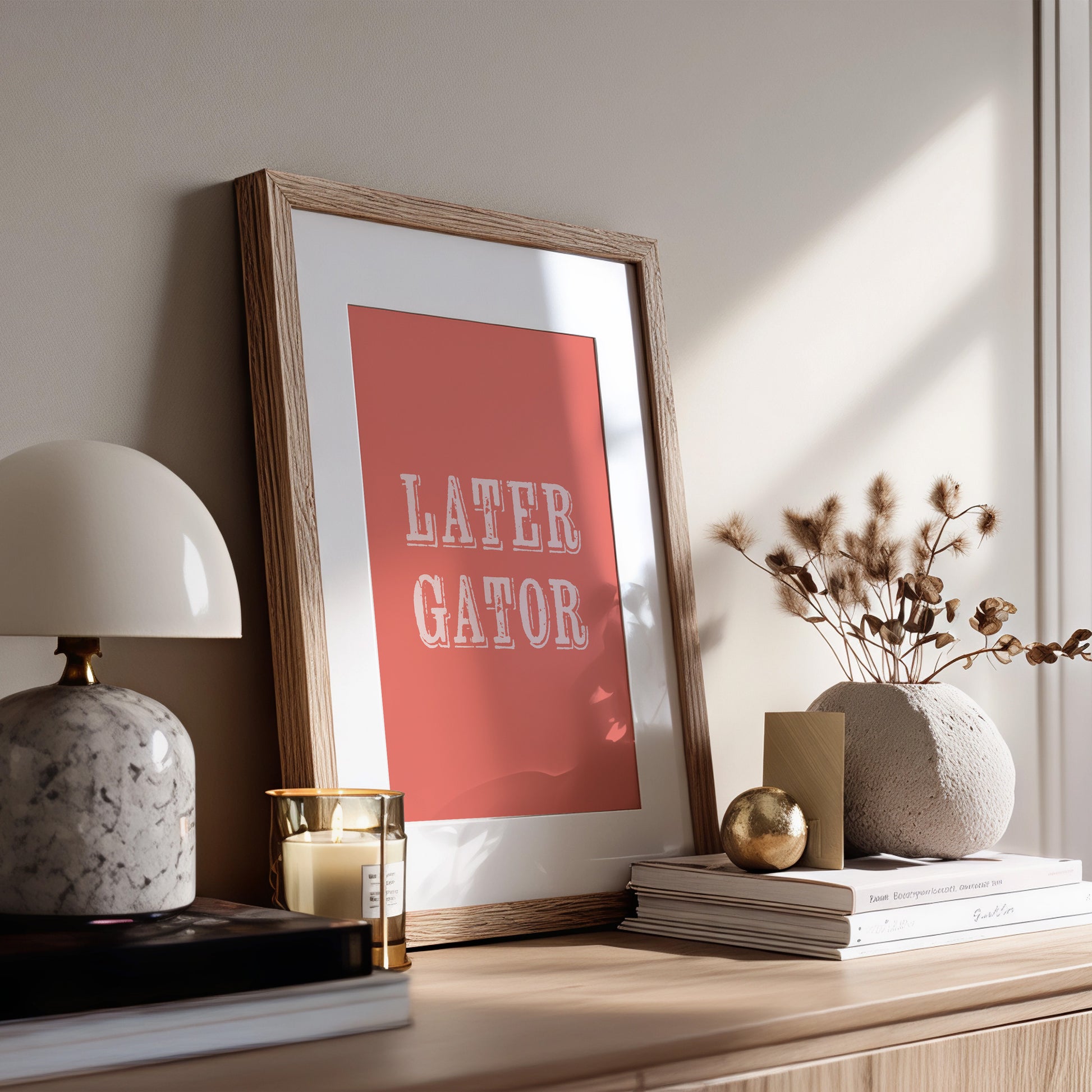 Framed print with 'LATER GATOR' text on a shelf with decorative items