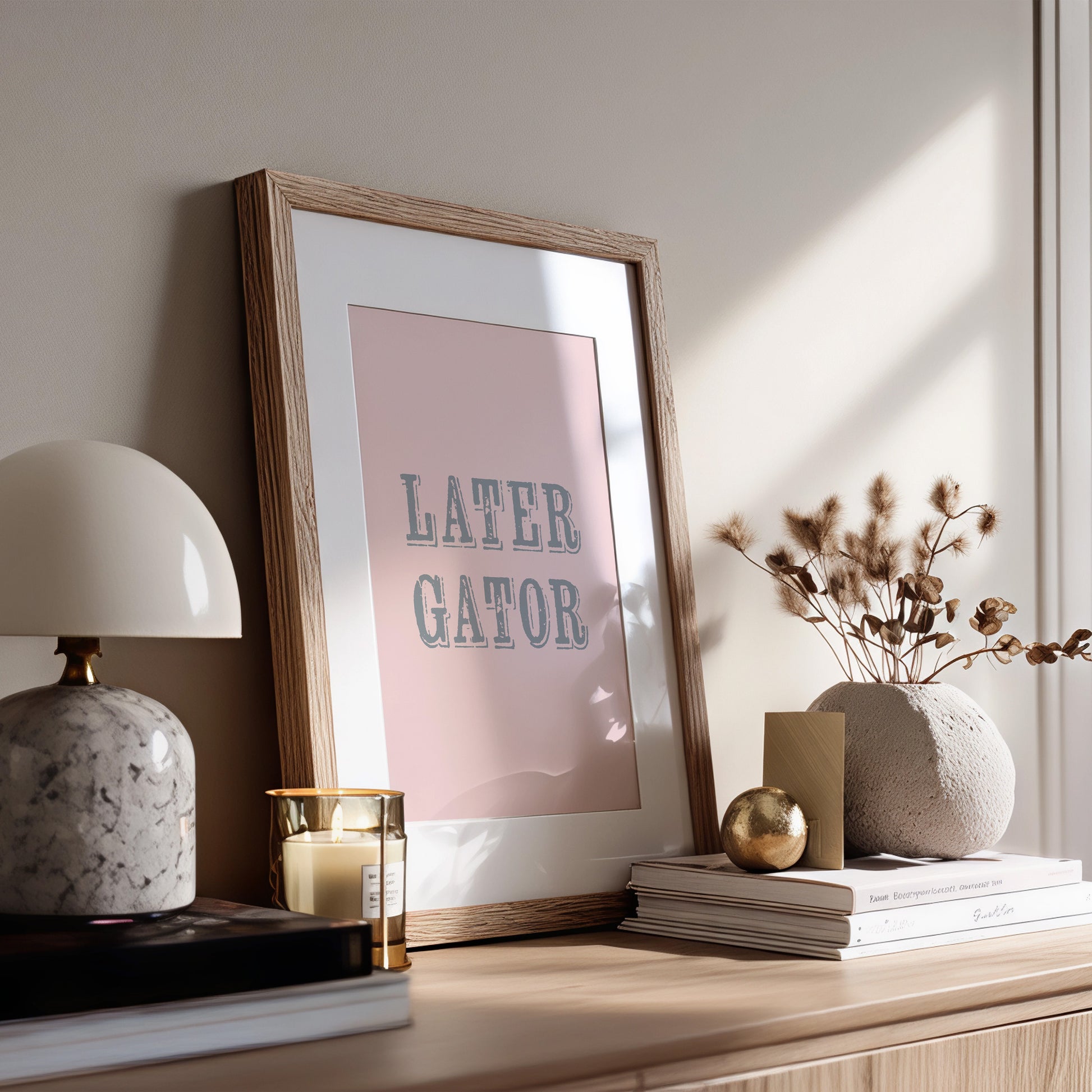Framed print with 'LATER GATOR' text on a shelf with decor items