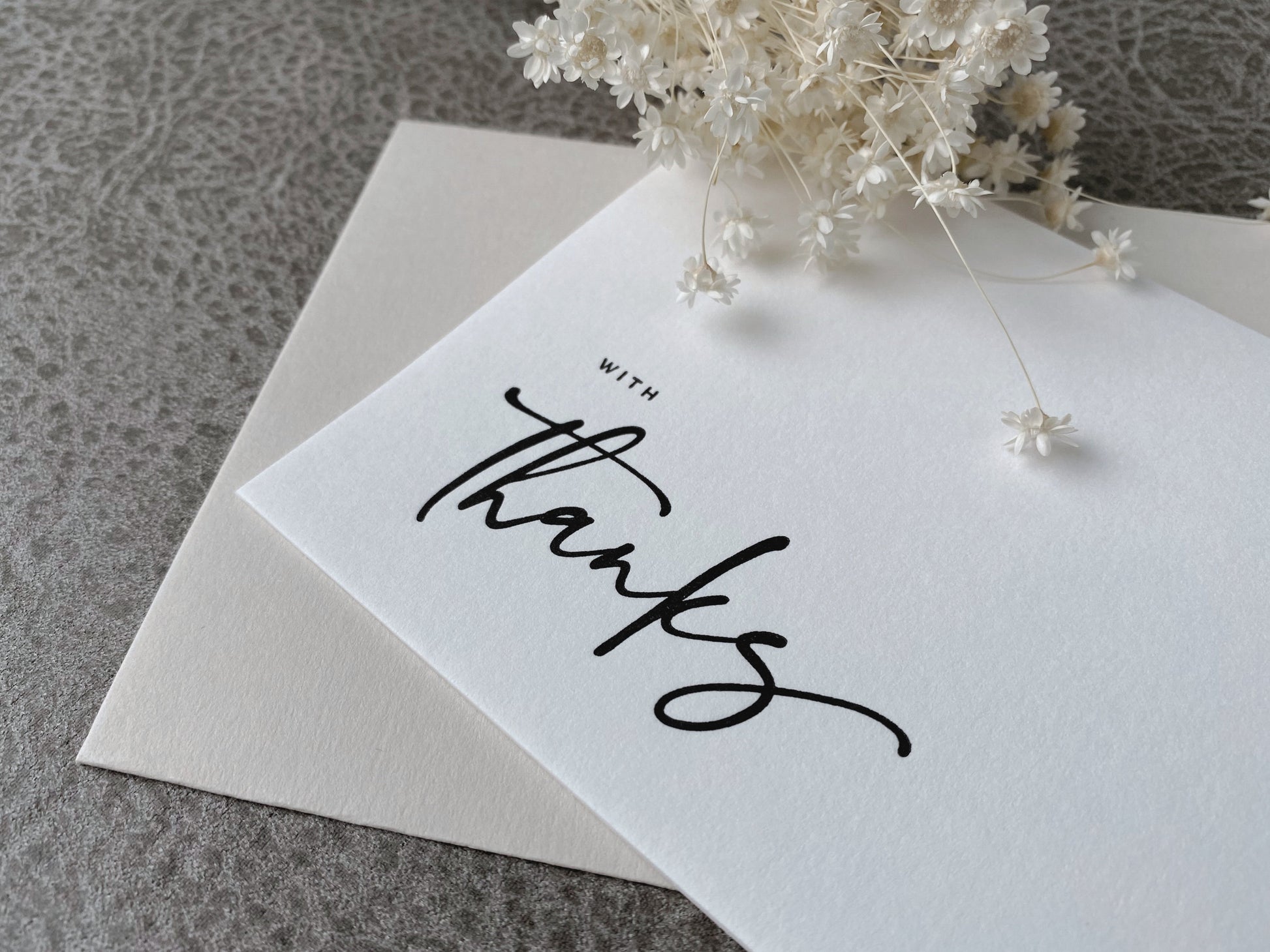 A white letterpress greeting card with the phrase 'With Thanks' printed in black, accompanied by a premium envelope.