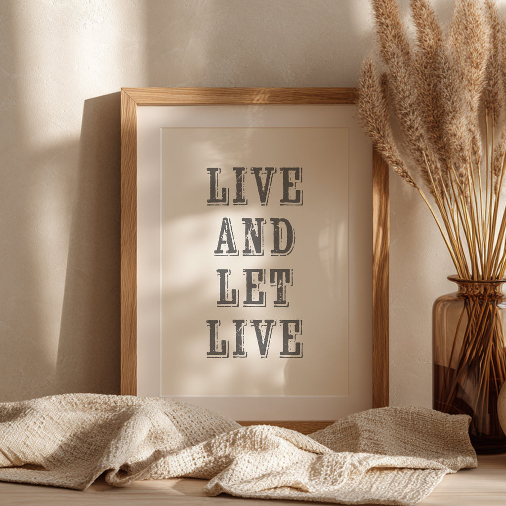 Framed art print with the phrase 'Live and Let Live' leaning against a wall on a sideboard
