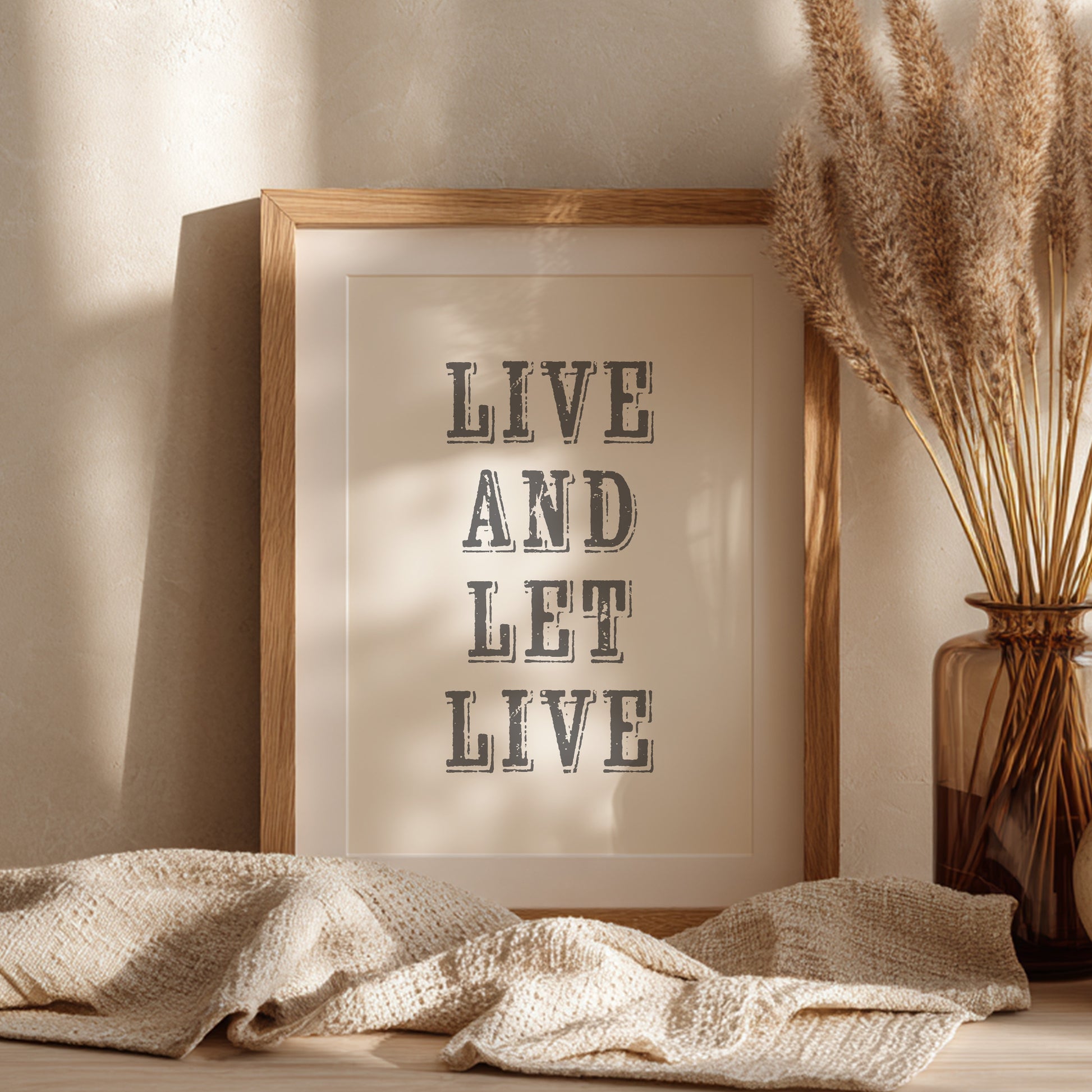 Framed art print with the phrase 'Live and Let Live' leaning against a wall on a sideboard