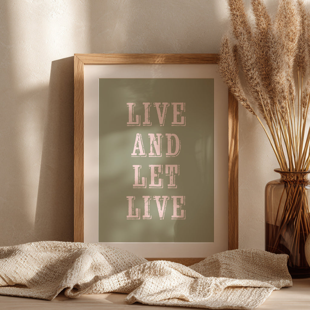 Framed art print with the phrase 'Live and Let Live' leaning against a wall on a sideboard