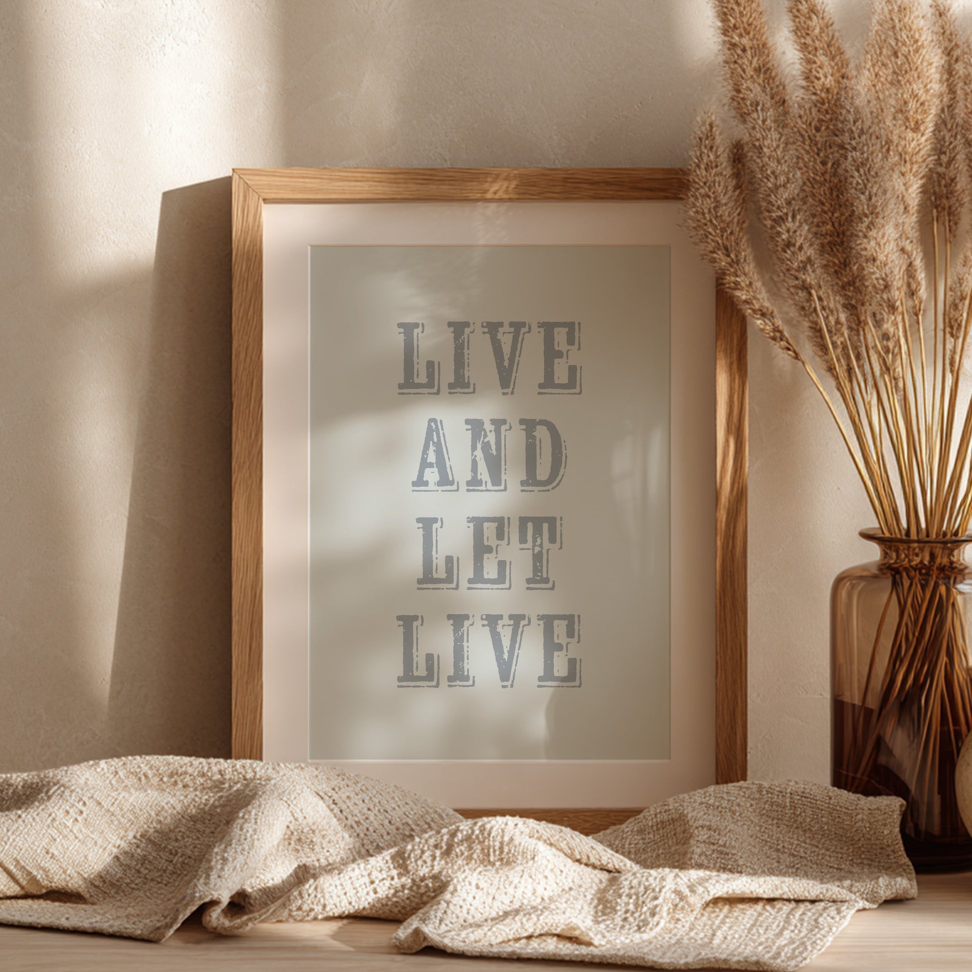 Framed art print with the phrase 'Live and Let Live' leaning against a wall on a sideboard
