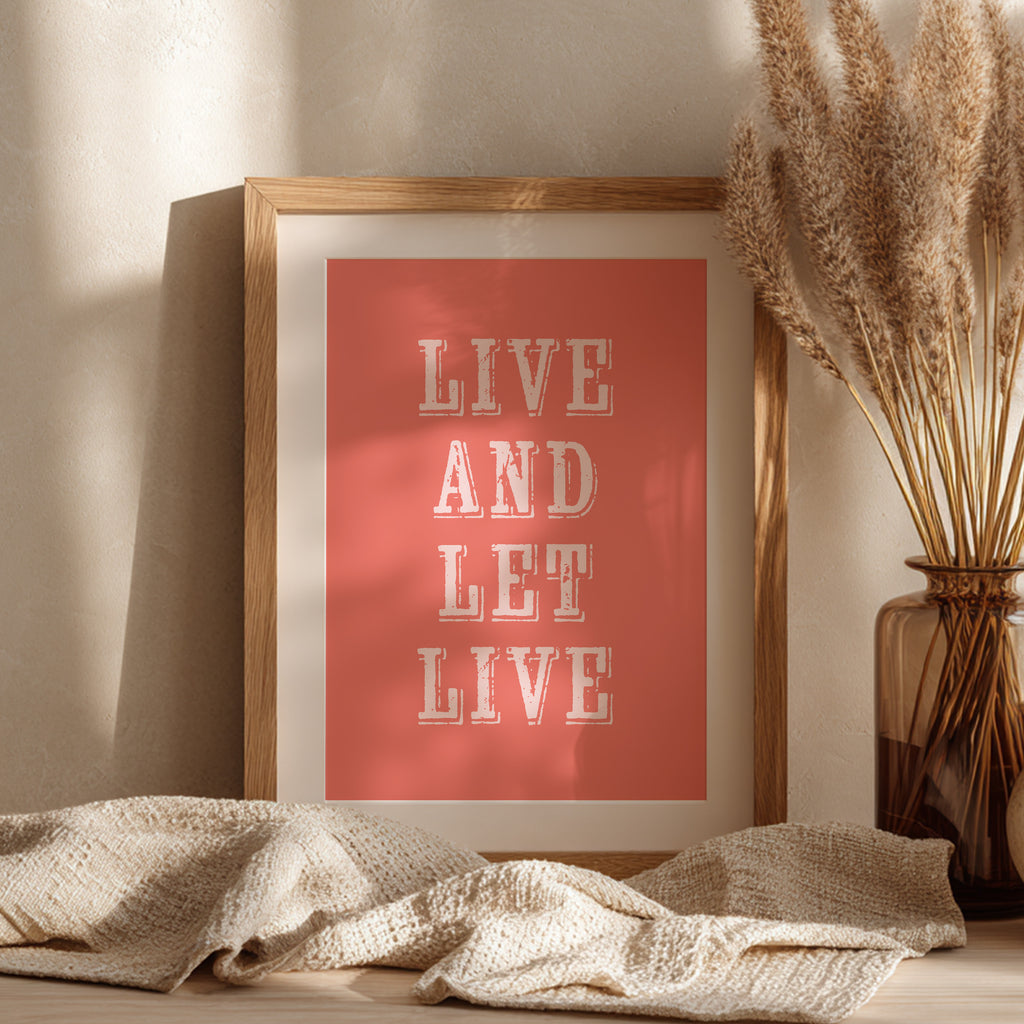 Framed art print with the phrase 'Live and Let Live' leaning against a wall on a sideboard