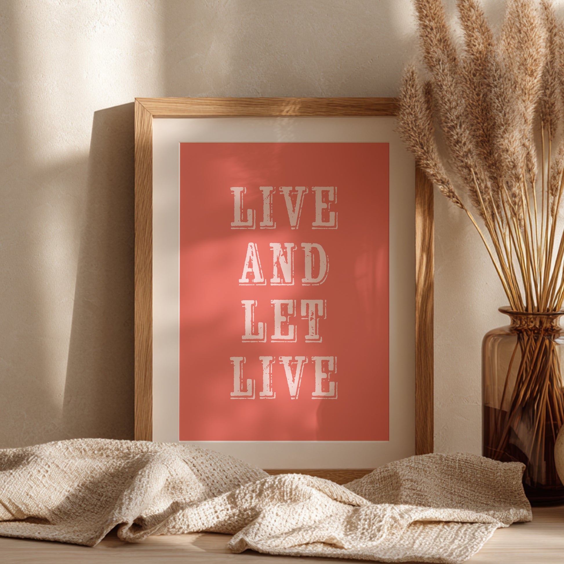 Framed art print with the phrase 'Live and Let Live' leaning against a wall on a sideboard