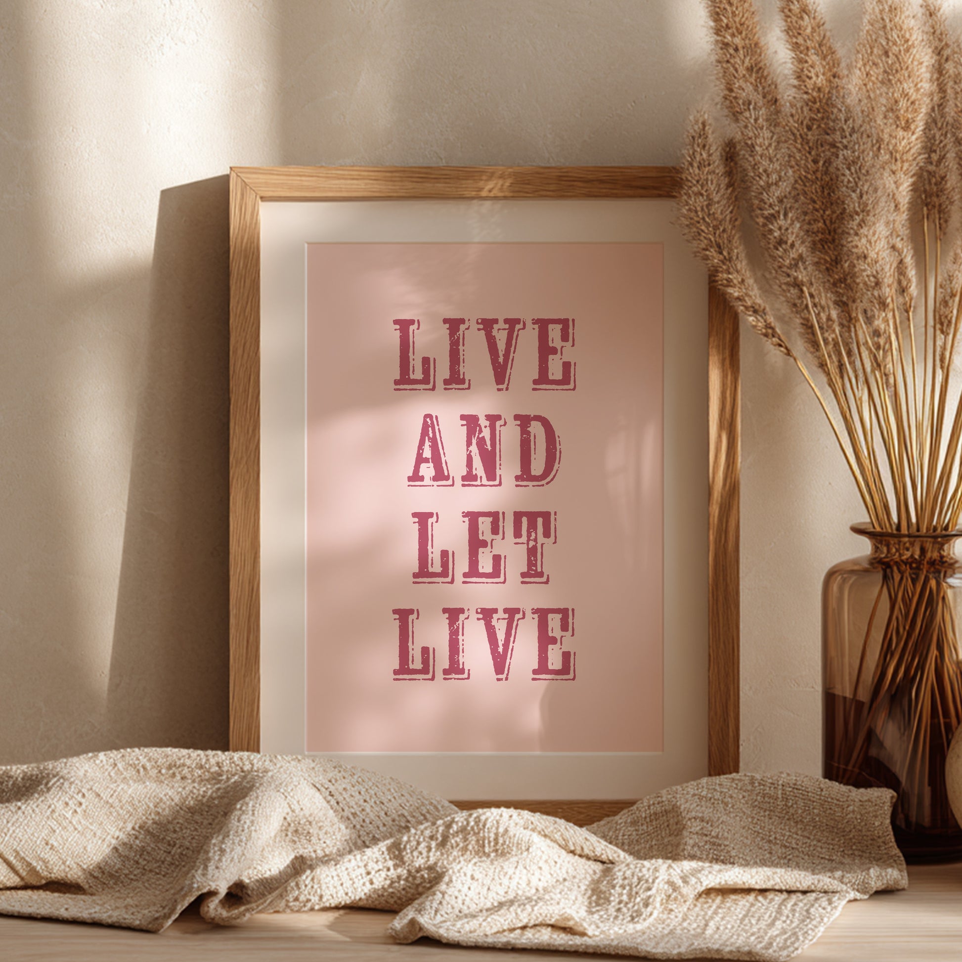 Framed art print with the phrase 'Live and Let Live' leaning against a wall on a sideboard