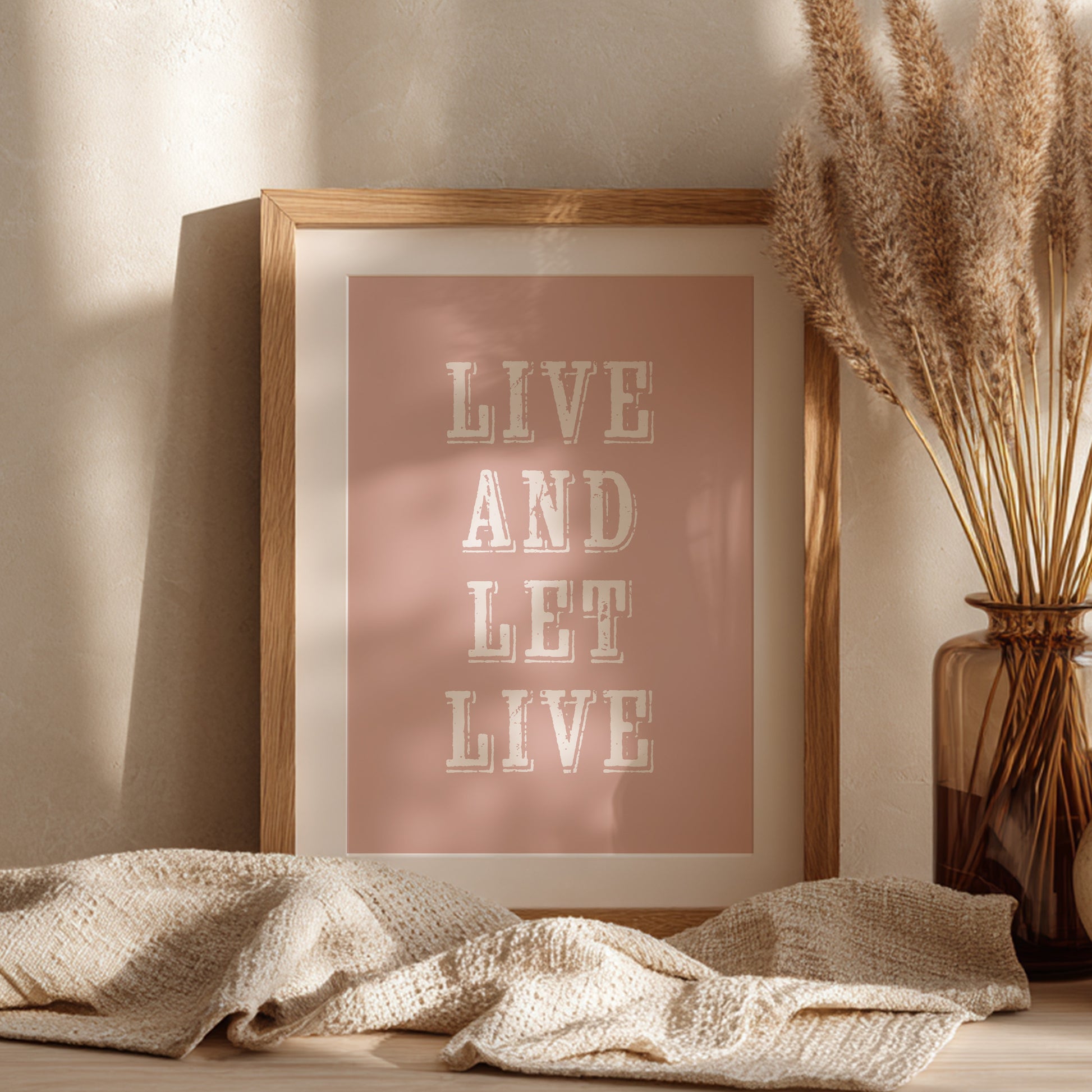 Framed art print with the phrase 'Live and Let Live' leaning against a wall on a sideboard