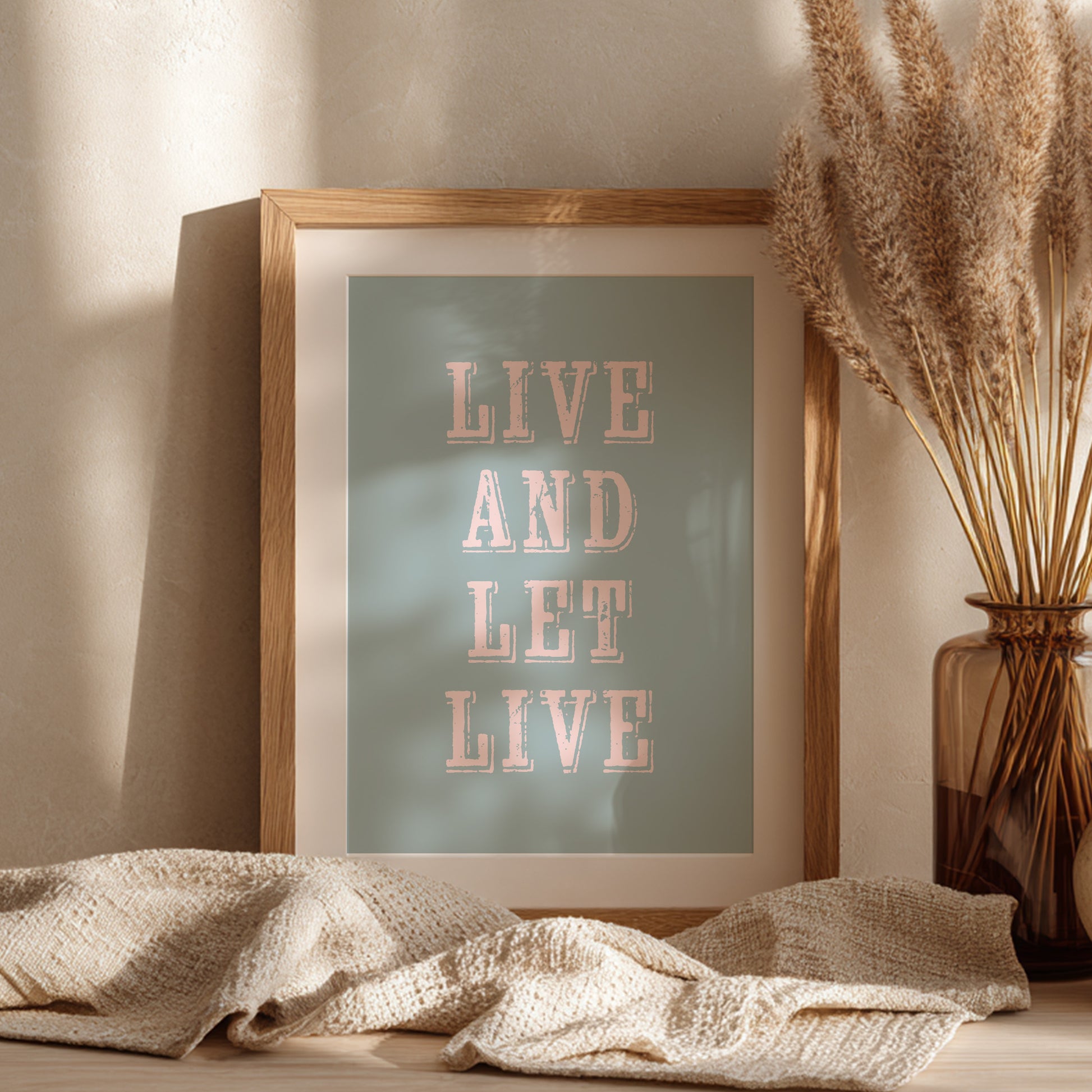 Framed art print with the phrase 'Live and Let Live' leaning against a wall on a sideboard